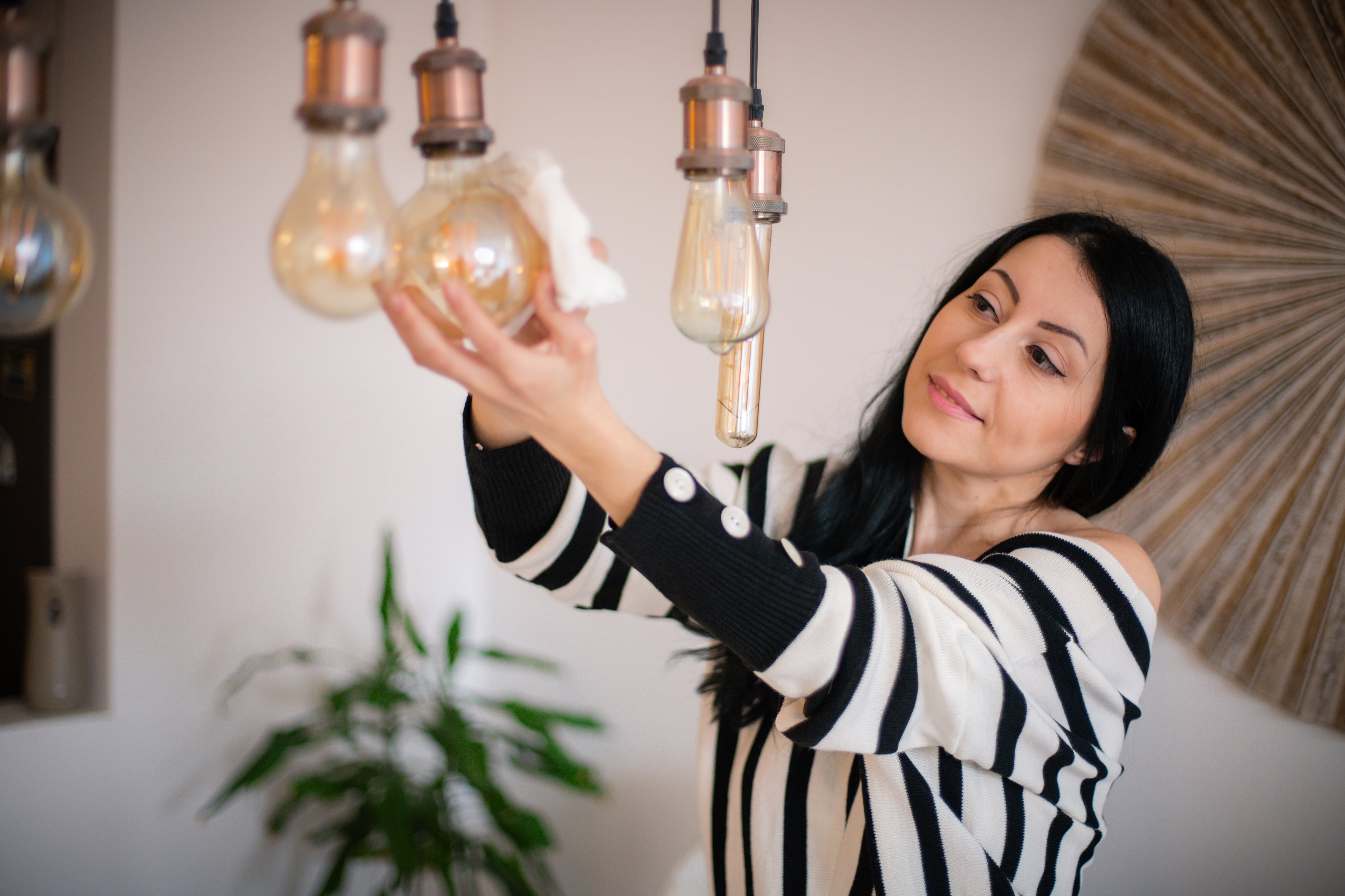 A woman dusting off light fixtures in her home