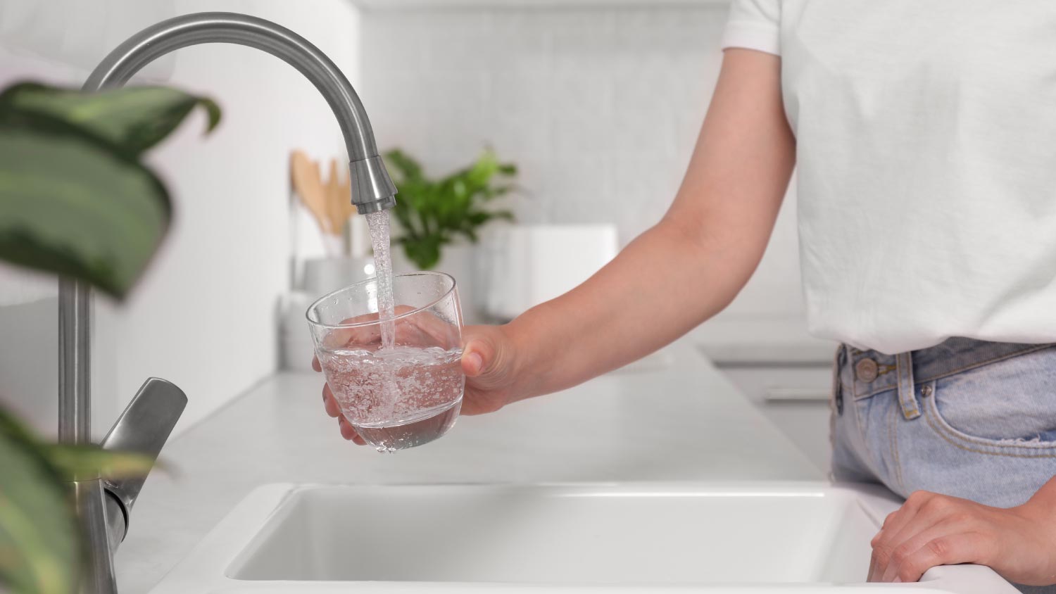 Woman filling glass with water from tap in kitchen