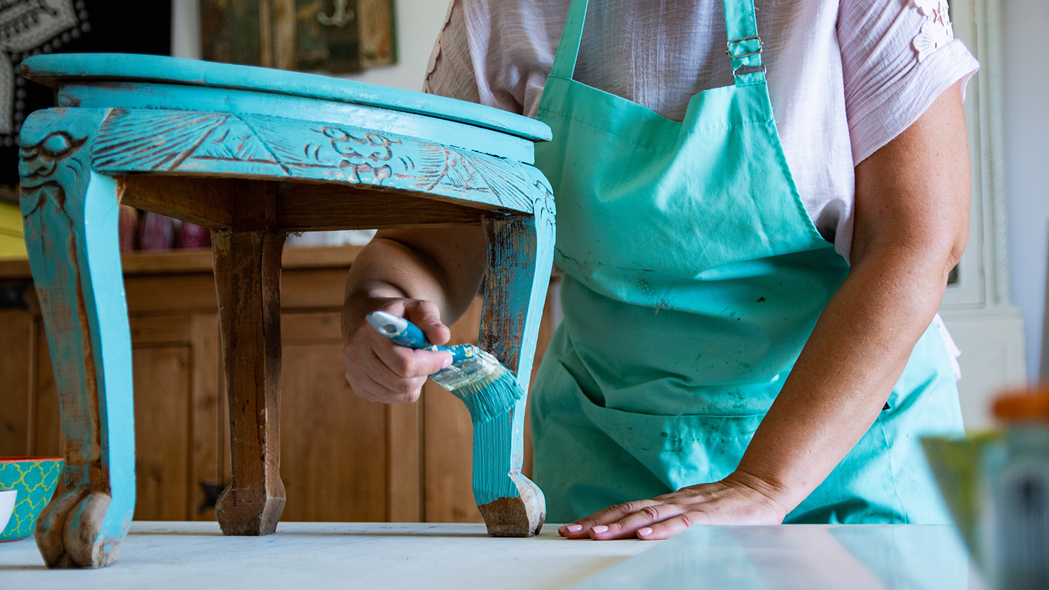 Woman repainting a piece of antique furniture blue