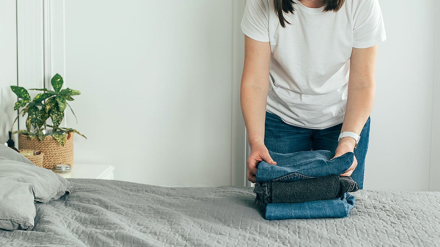 Woman folding jeans on her bed