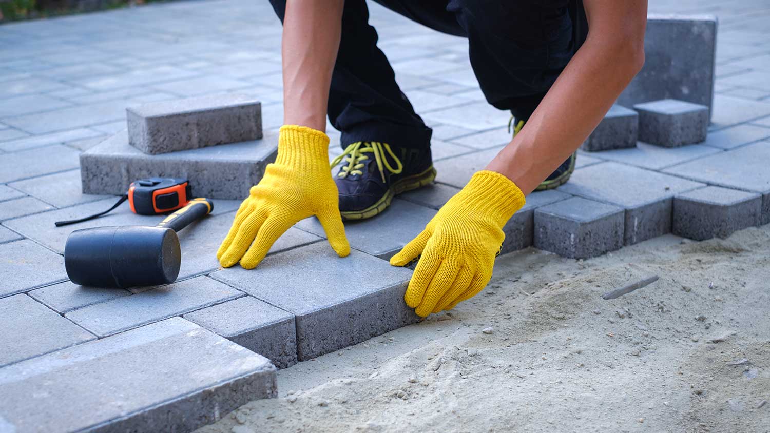 Worker laying pavers on sand foundation