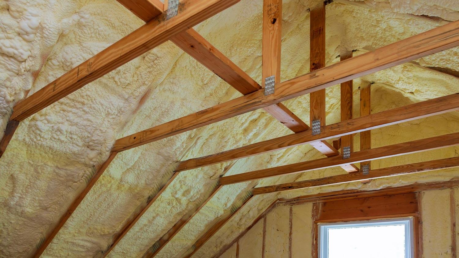 An attic with foam insulation between the wooden beams