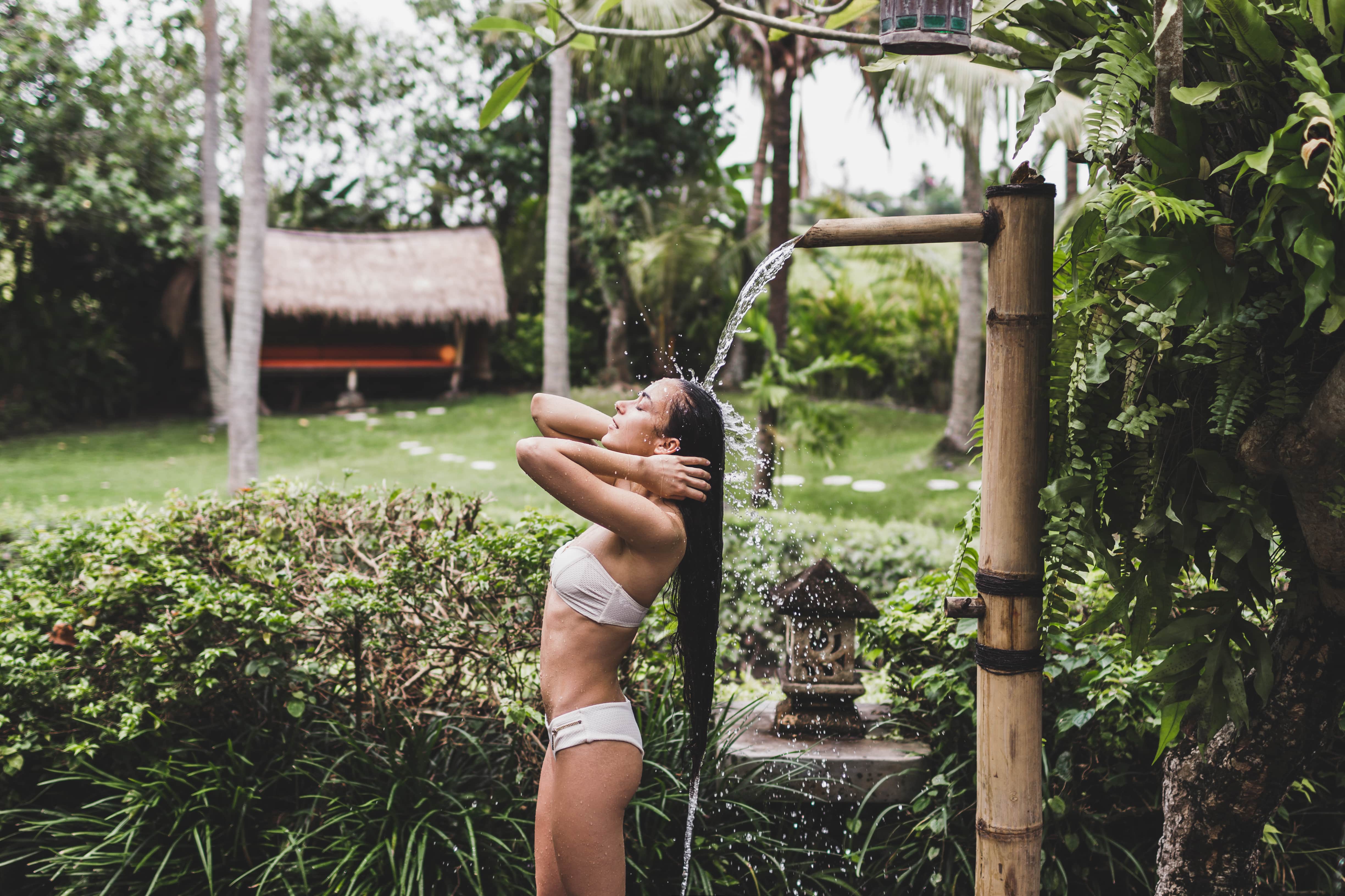 A woman in a two-piece bathing suit rinsing her hair in an outdoor shower