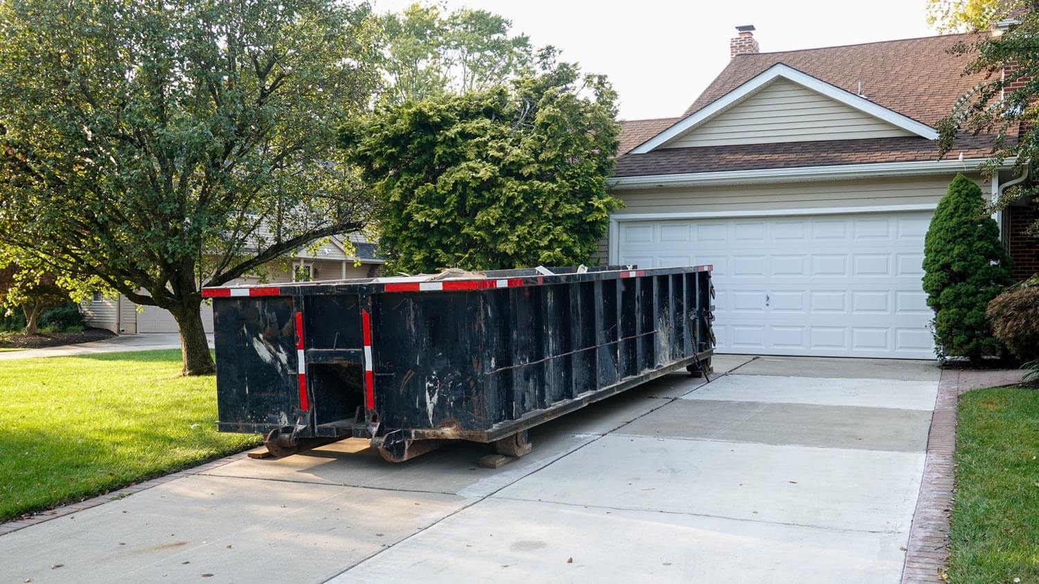 A big black dumpster in the driveway of a house