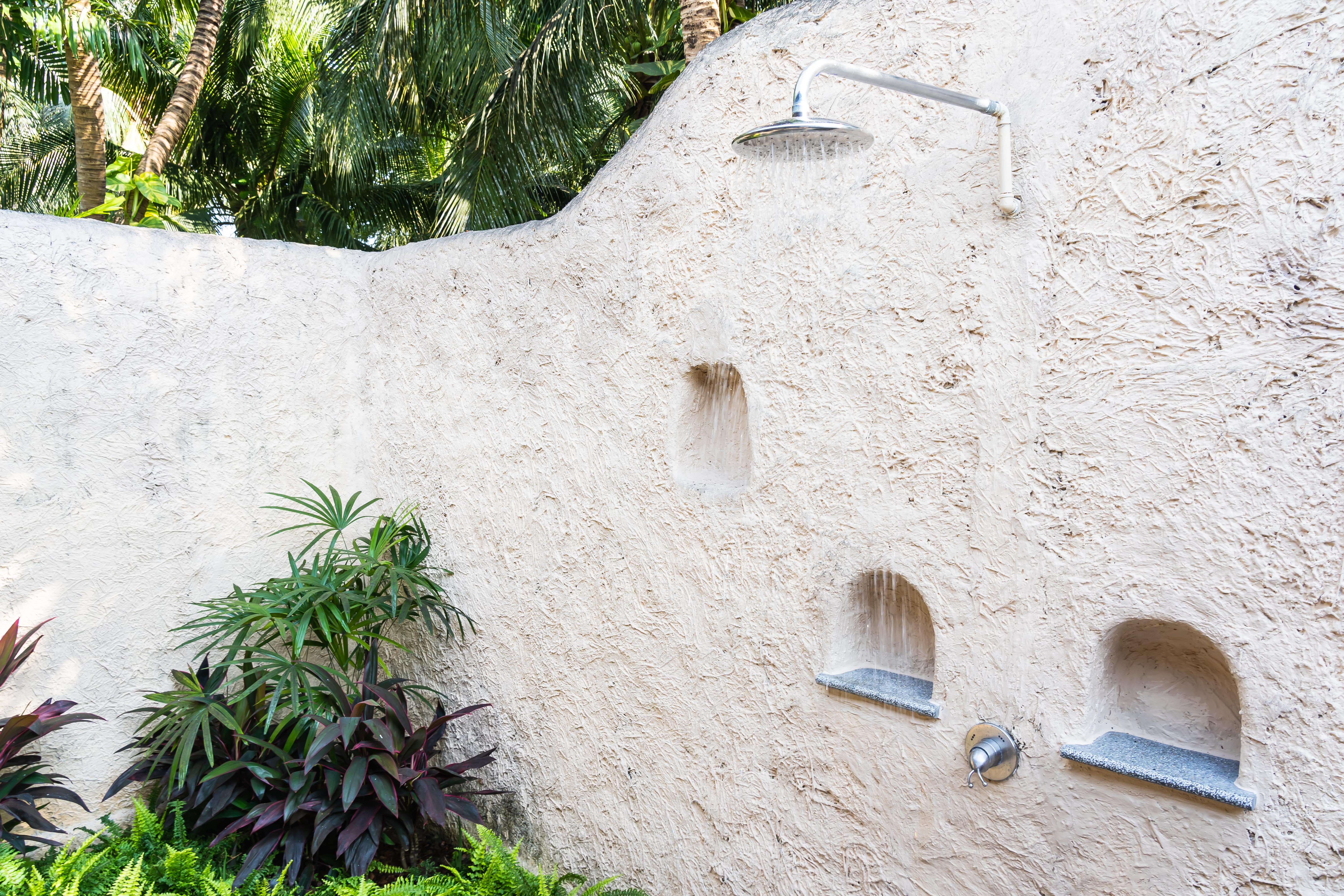 An outdoor shower with a tall stucco wall and built-in shelves