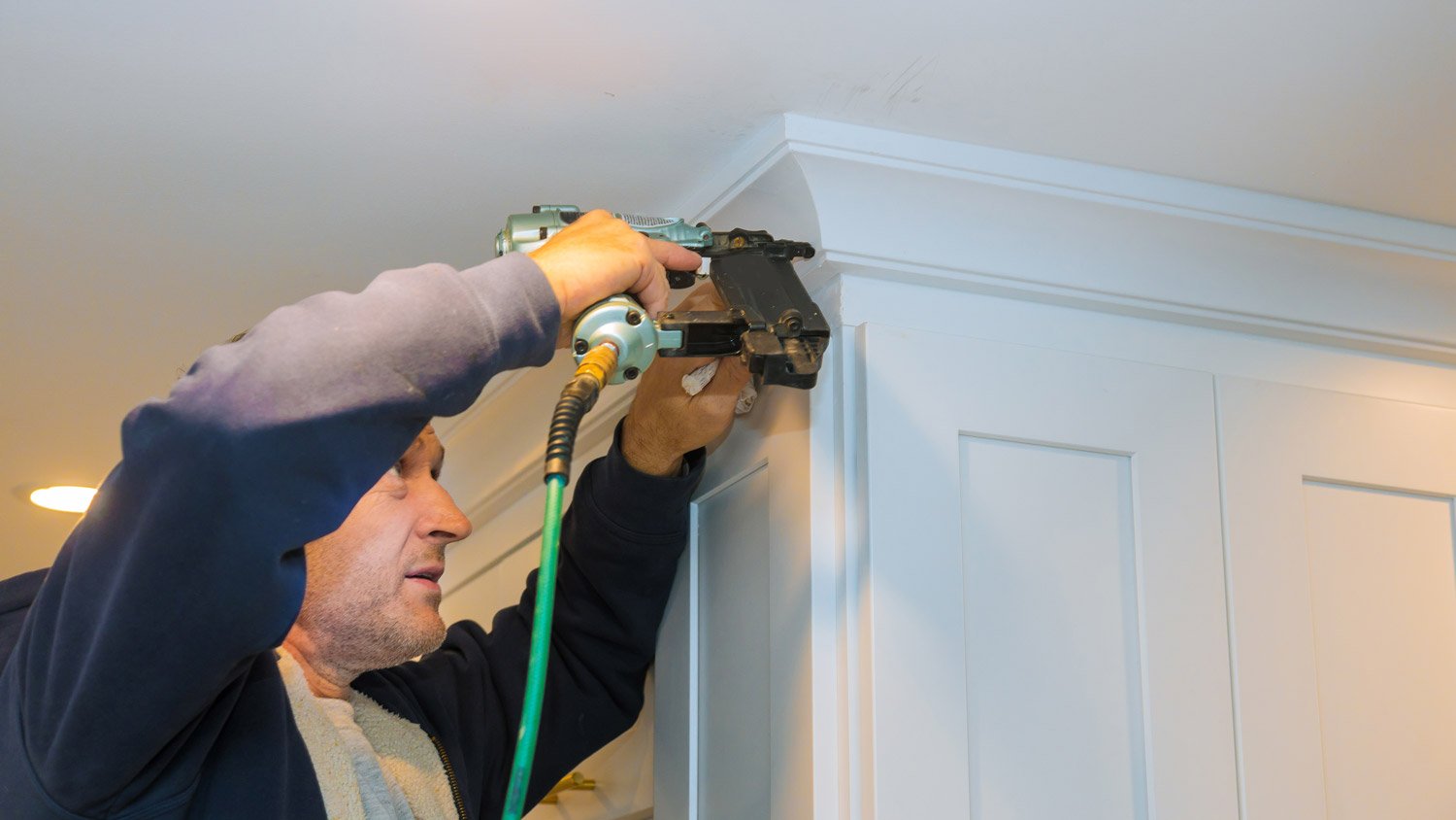 A carpenter adding crown molding to kitchen cabinets
