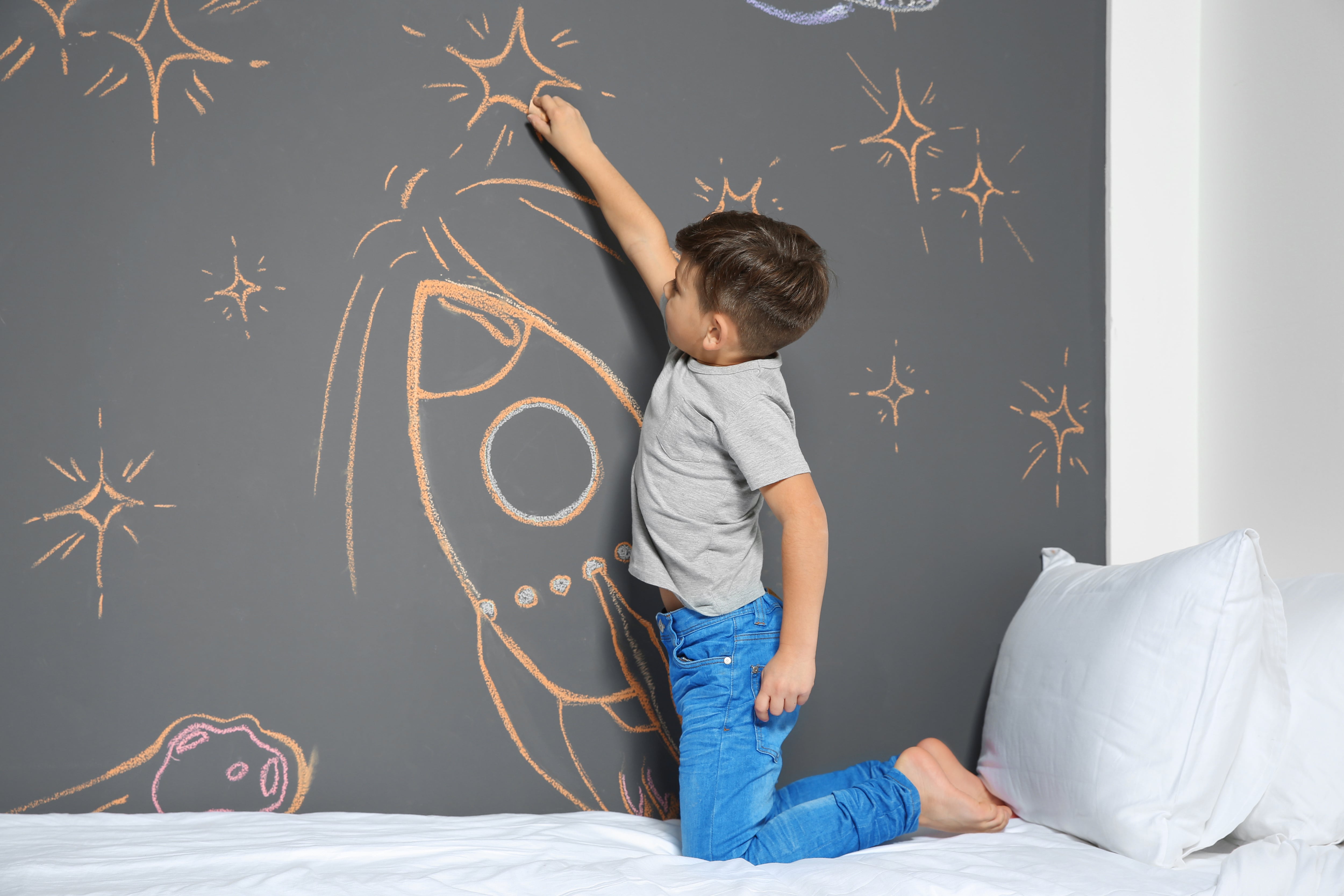 A young boy drawing on a chalkboard wall in a bedroom