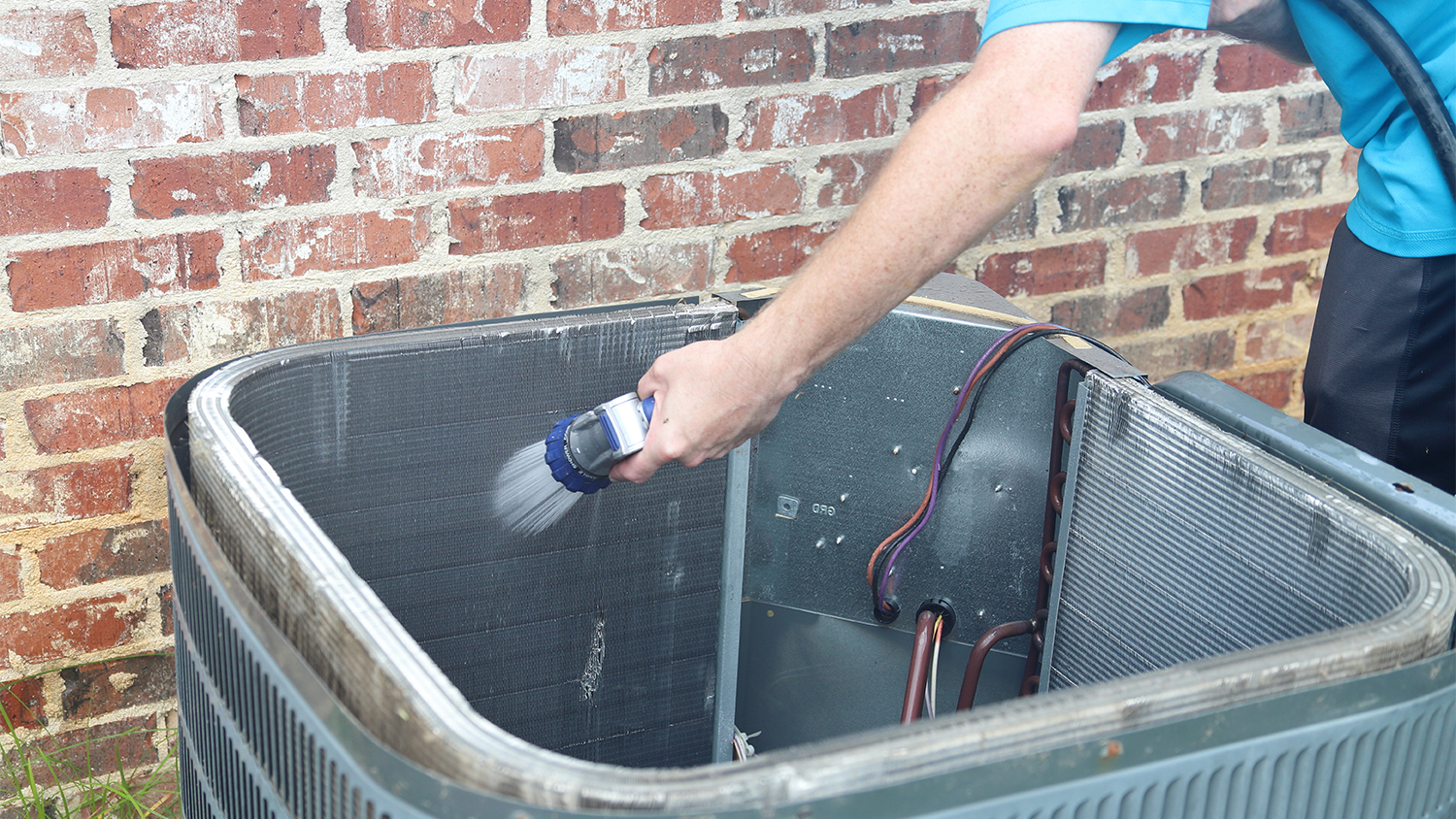 man cleaning coils of air conditioner with hose 