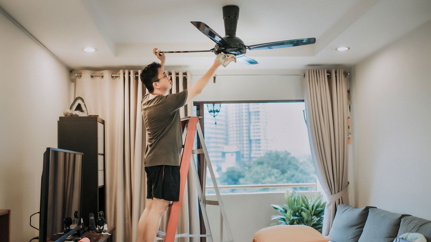 Young man on a lather cleaning ceiling fan 