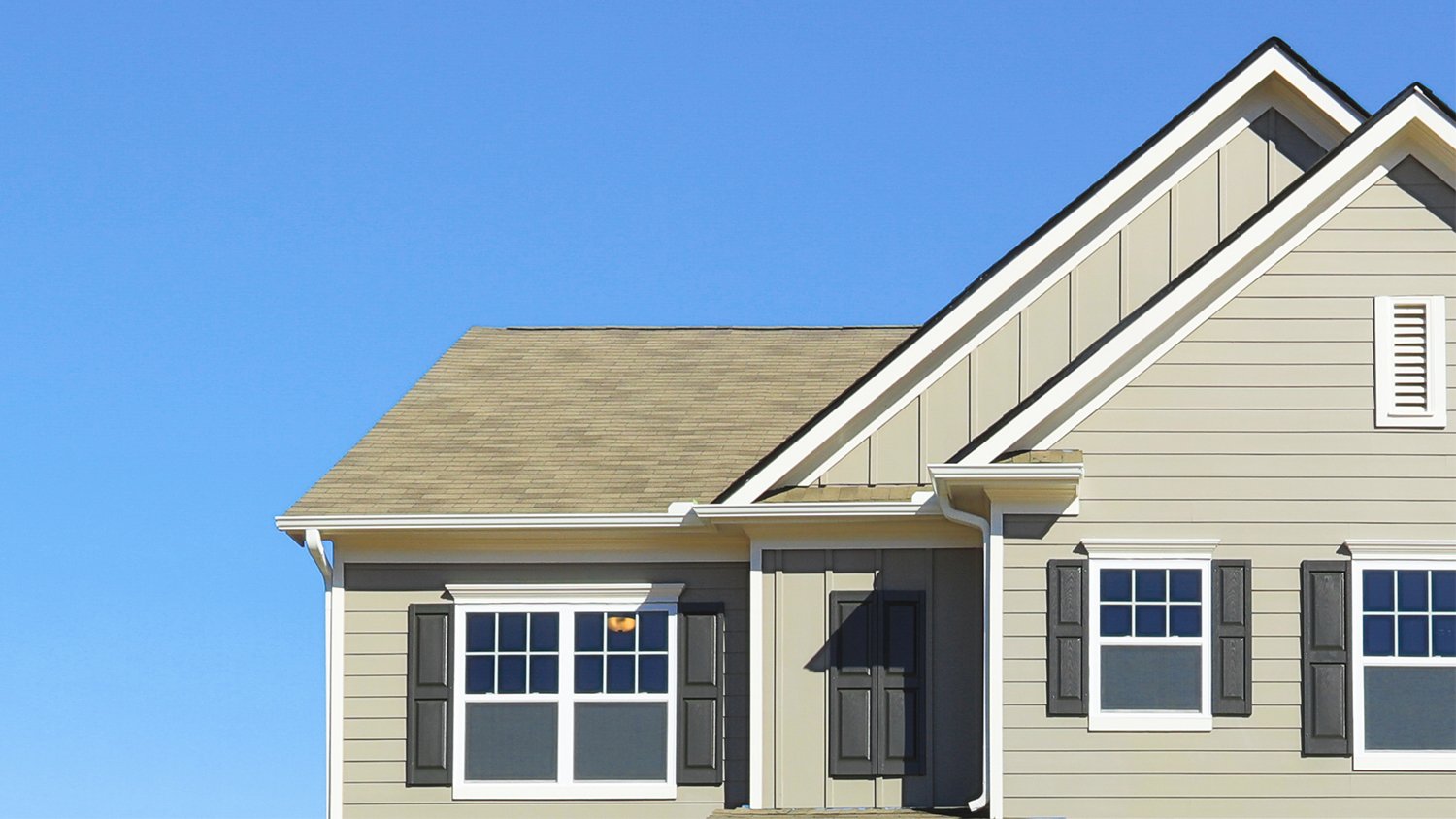 Closeup of house rooftop with brown siding and black shutters