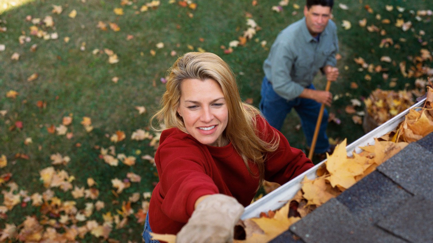 Couple removing autumn leaves from gutters