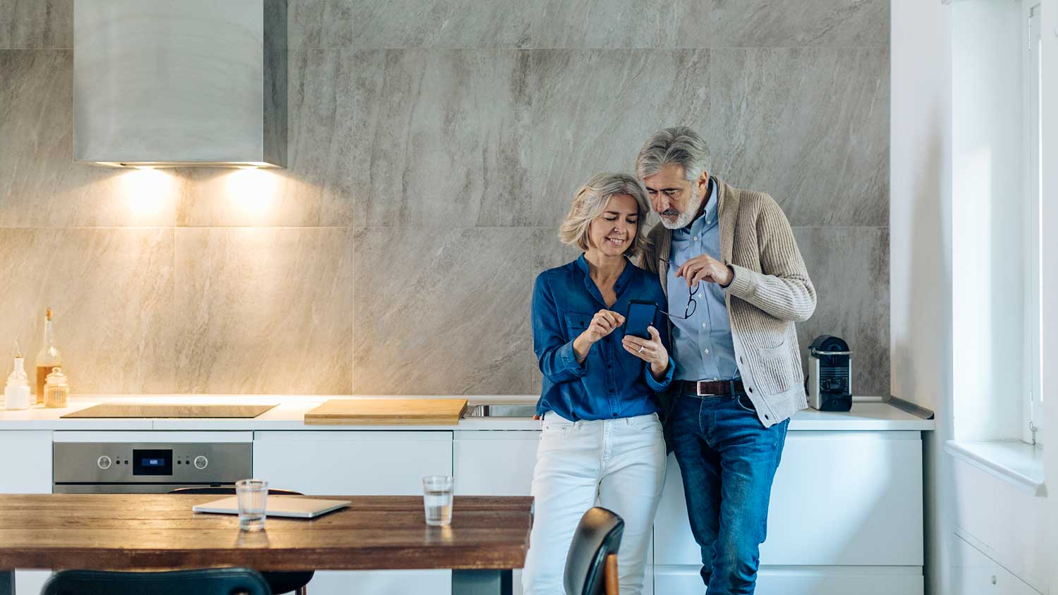 Mature couple in a minimalist kitchen using phone