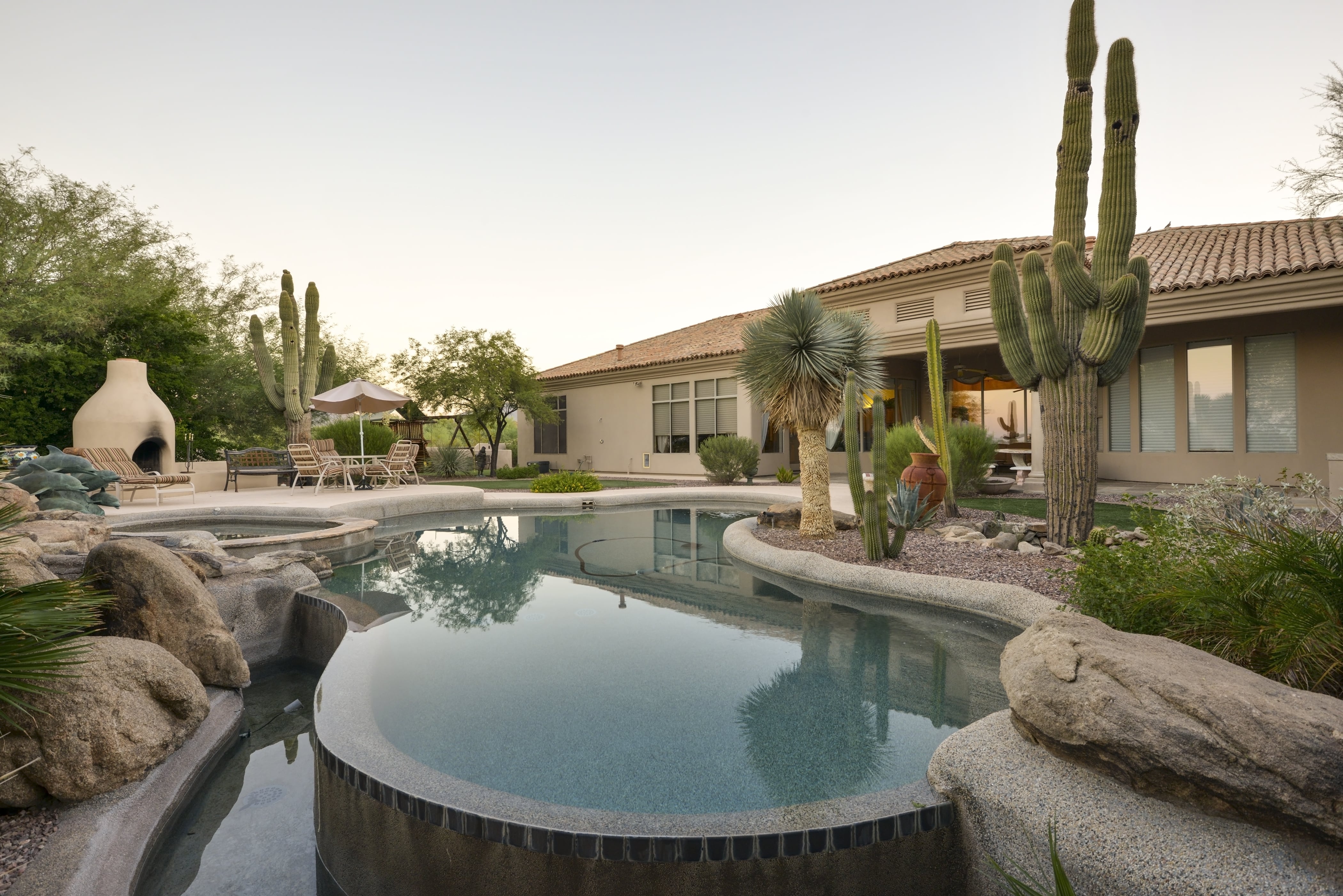 A desert backyard with an in-ground pool, cacti, a fire pit, and a table and chairs set