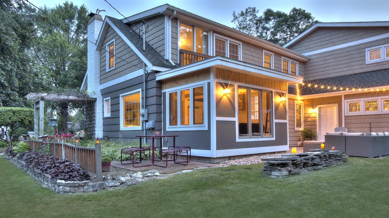 The exterior of a gray Cape Cod style house with its outdoor lights on