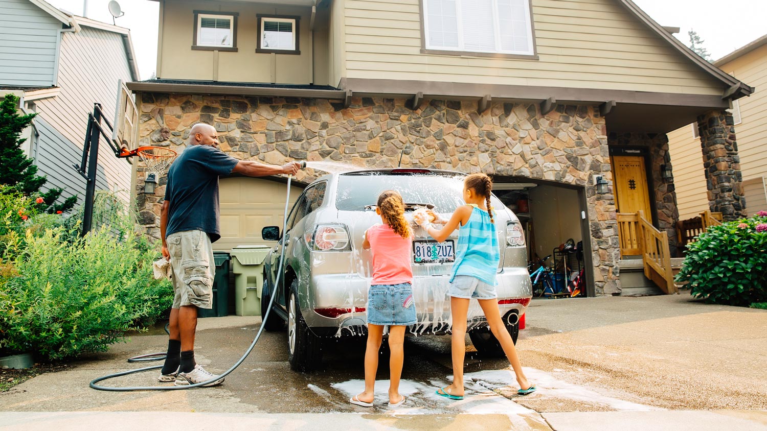 A father and his daughters washing the car in the driveway