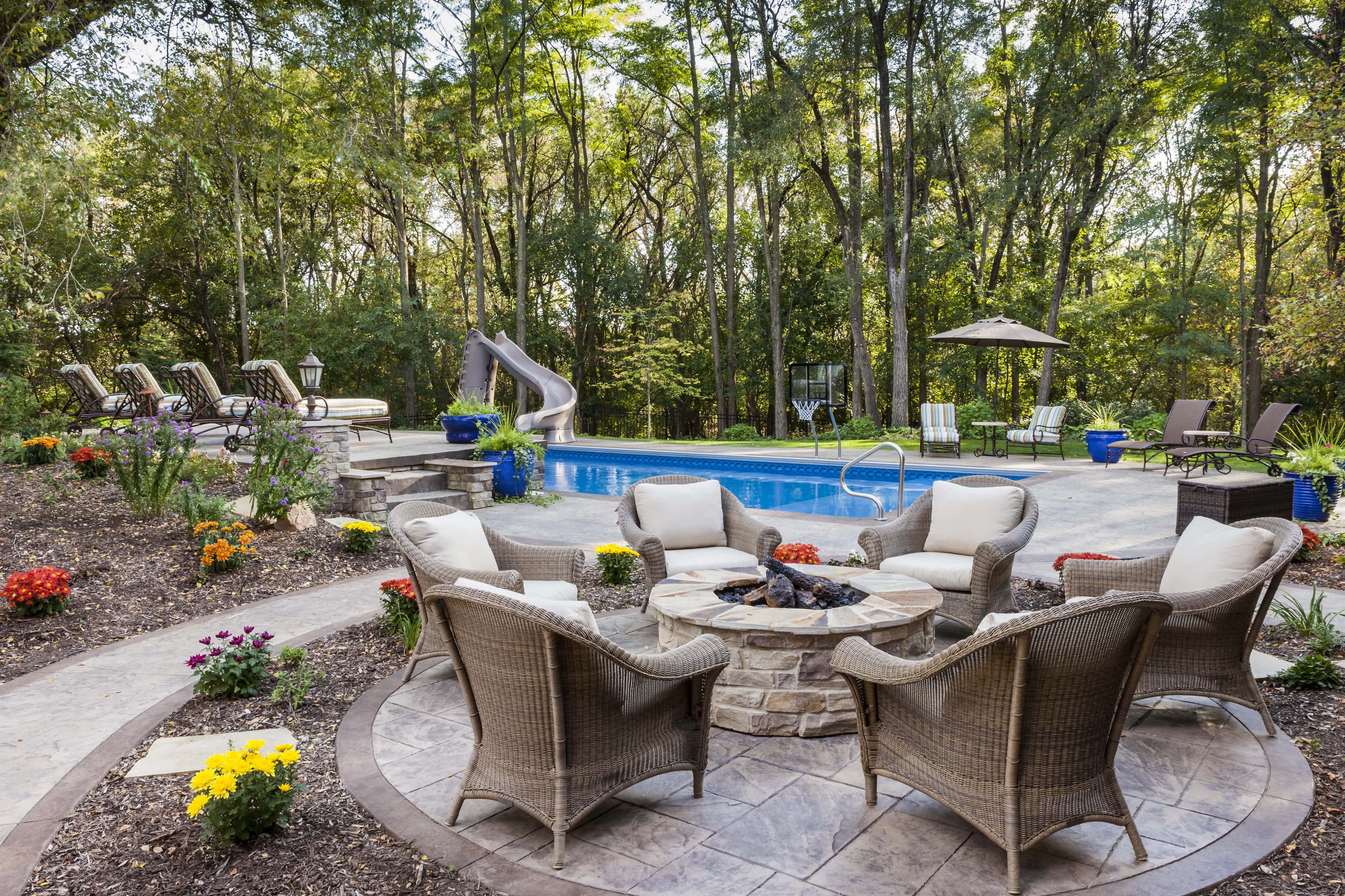 A backyard in-ground pool surrounded by grass, stone slabs, mulch, and flowers