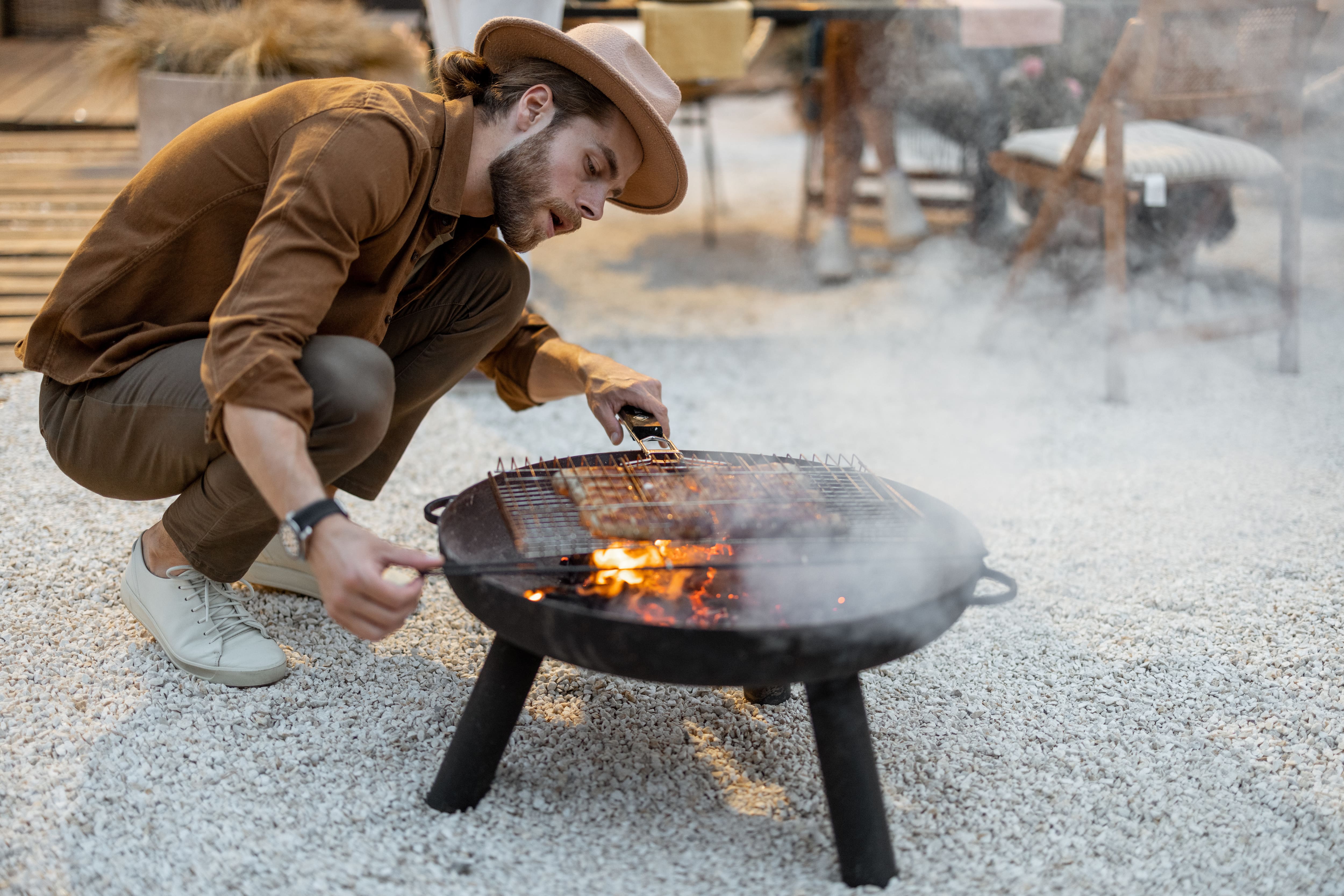 A man grilling food over a metal fire pit