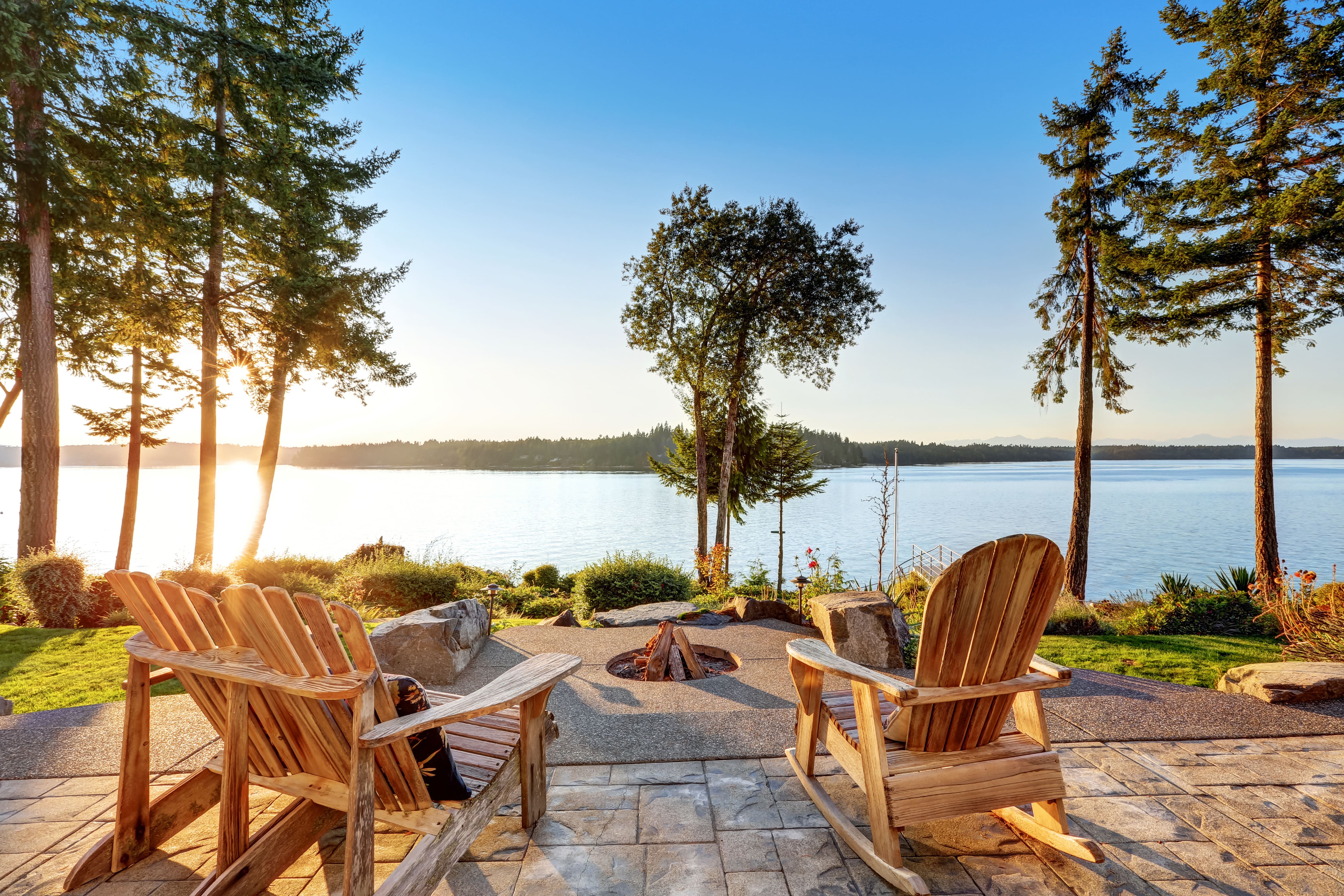 A lakeside fire pit with wood Adirondack chairs