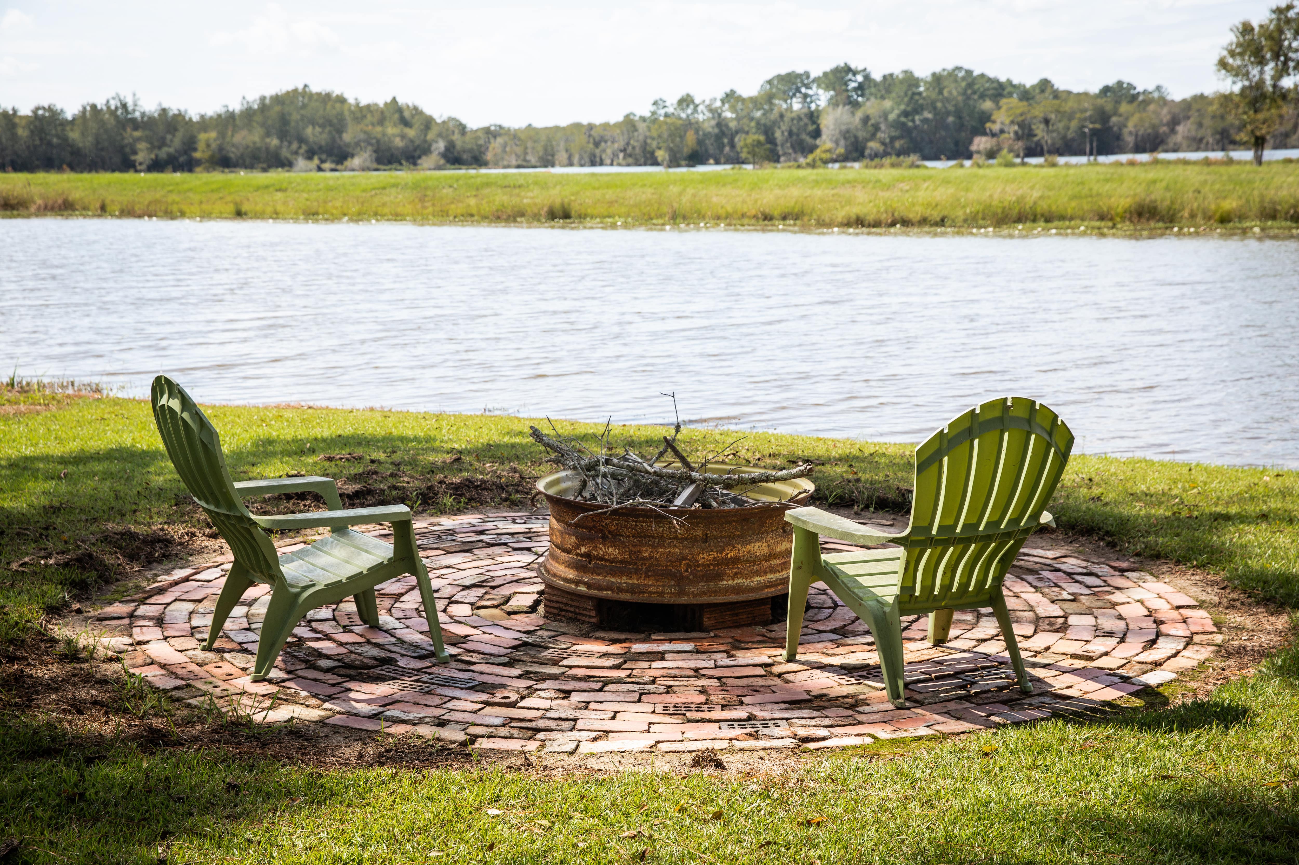 A lakeside fire pit made with an old car rim surrounded by Adirondack chairs