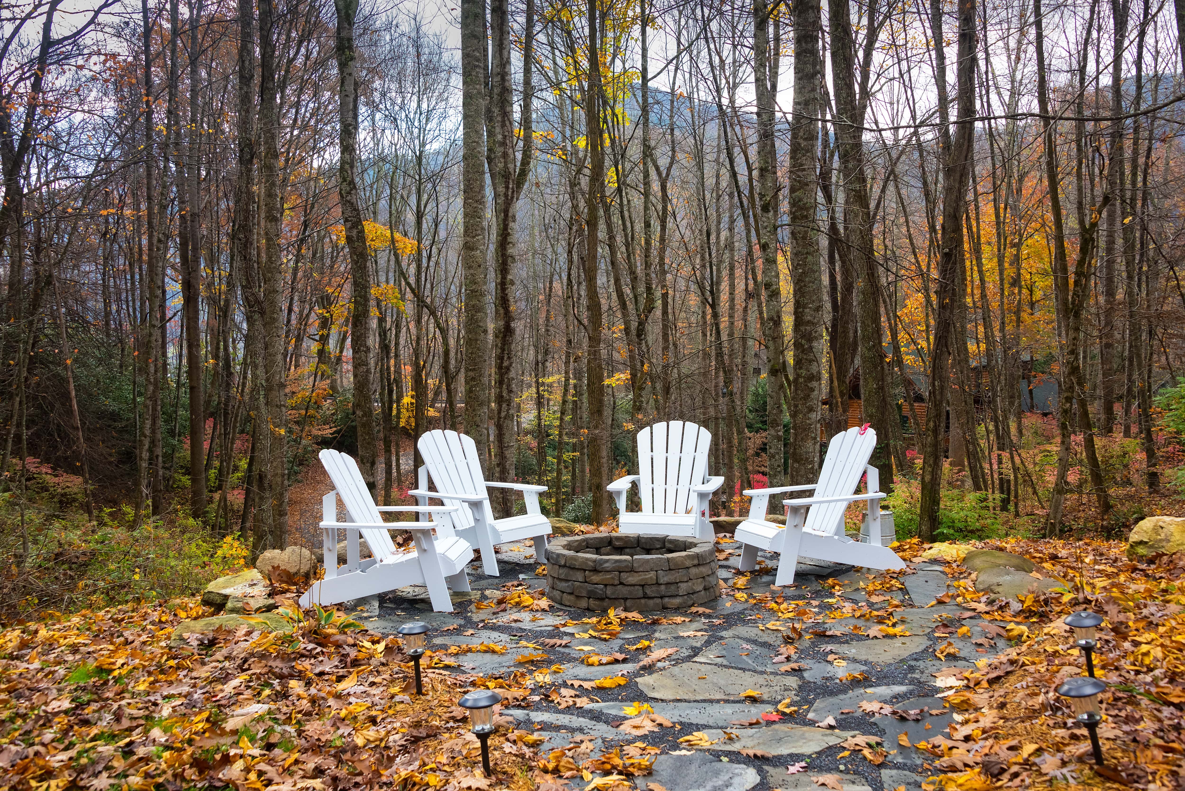 A round brick fire pit on a stone slab surrounded by Adirondack chairs