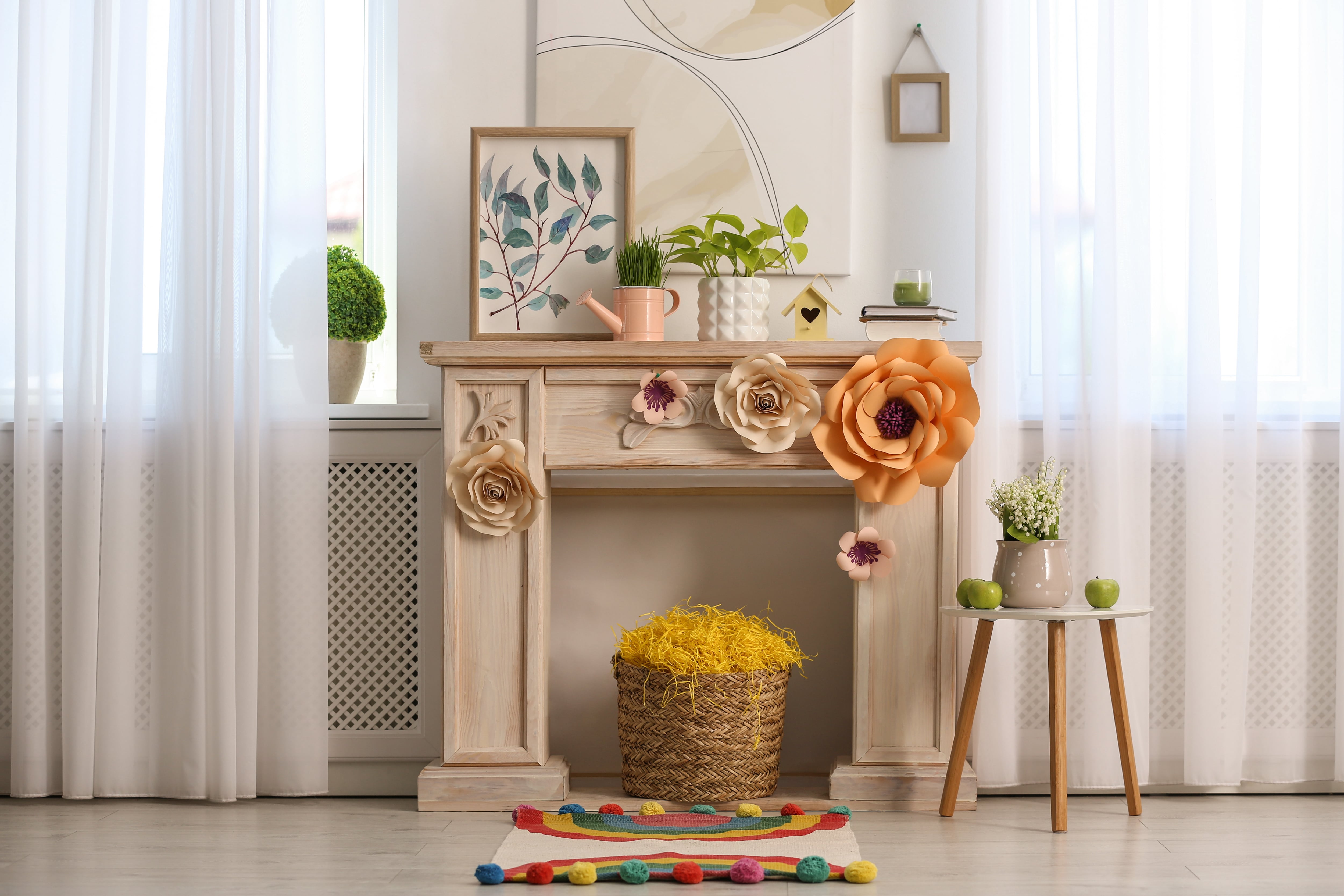 Fireplace mantel decorated with giant colorful paper flowers, green plants, and abstract art