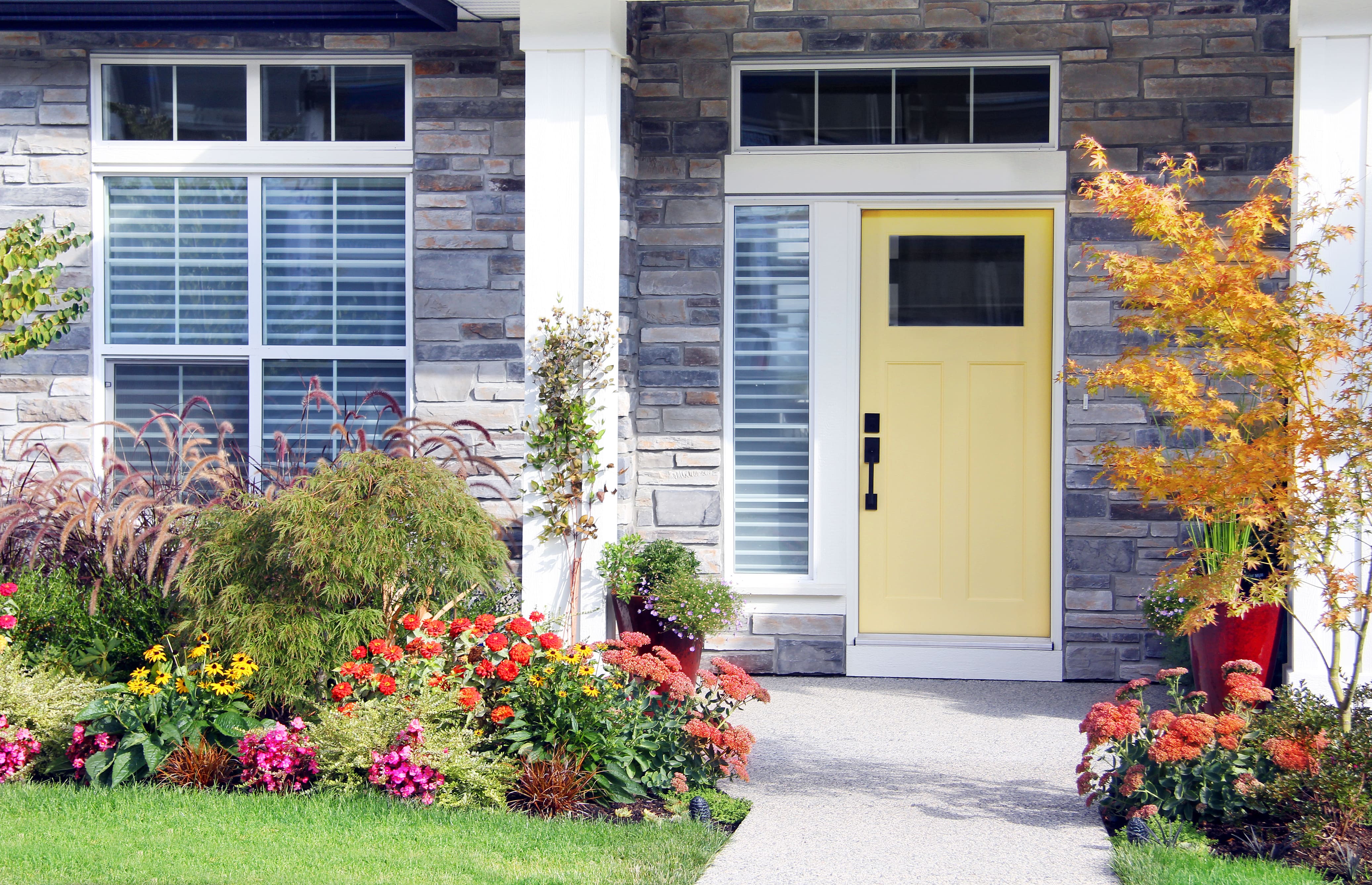 Colorful flowers in front of a gray brick home with a yellow door