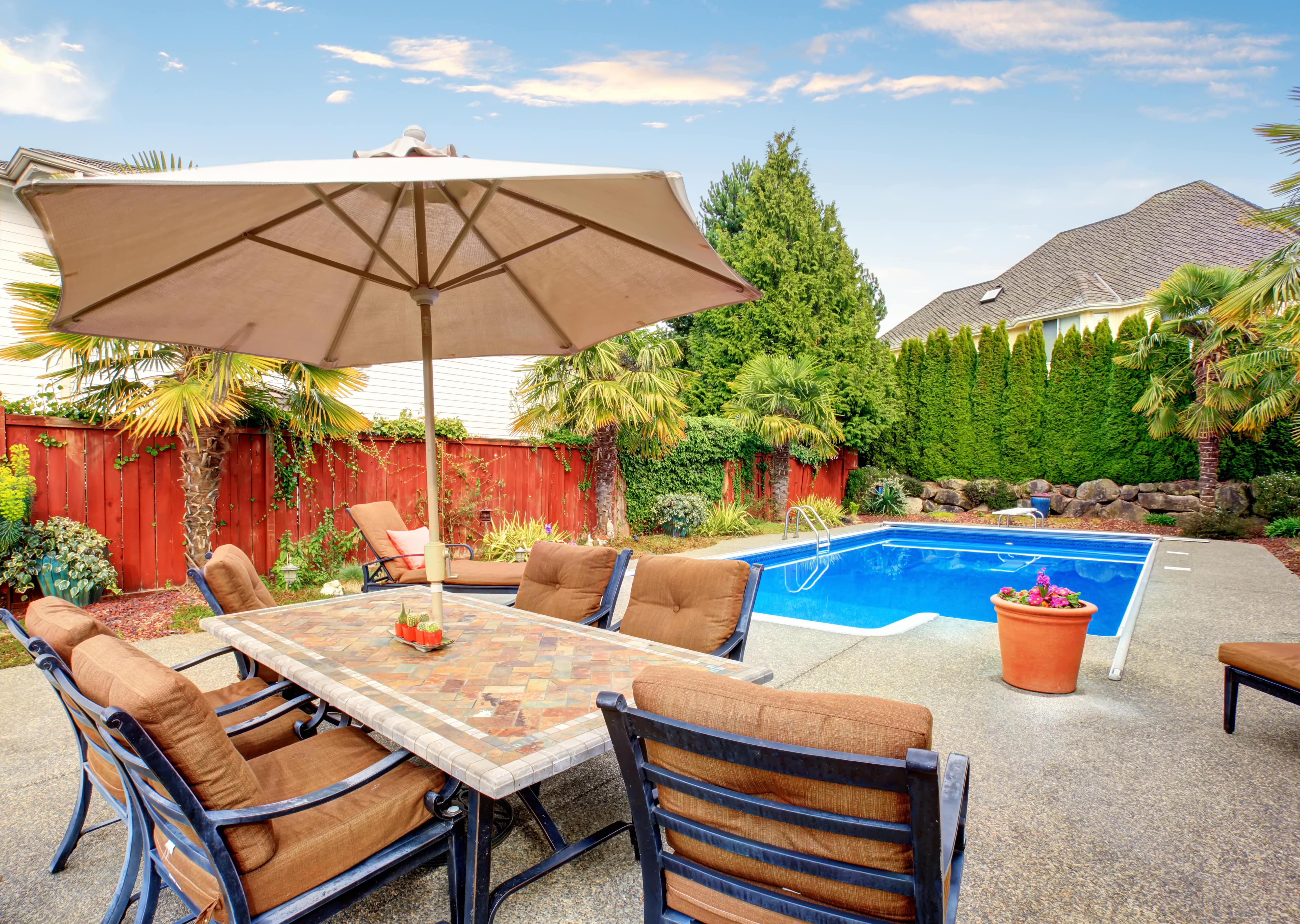 An in-ground pool with a backyard patio set, fencing, and tall trees for privacy