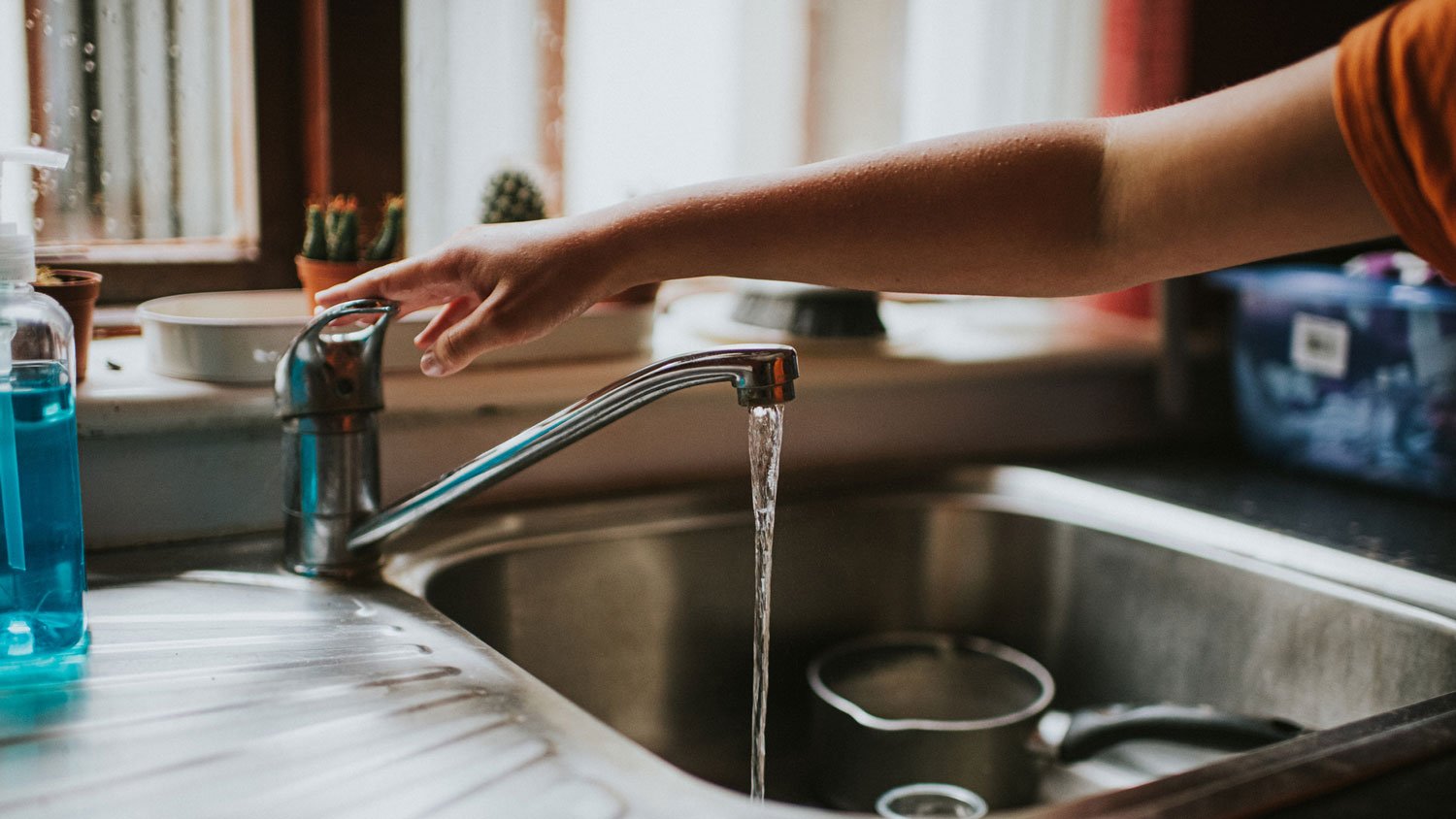 A woman’s hand turning off water in a shallow kitchen sink