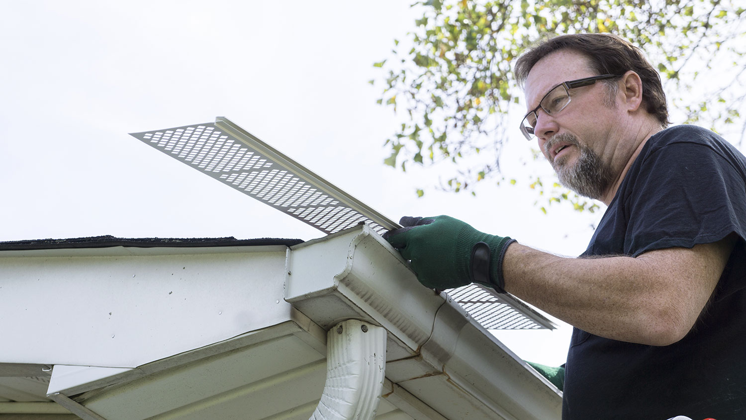 Handyman wearing protective gloves installing gutter guards