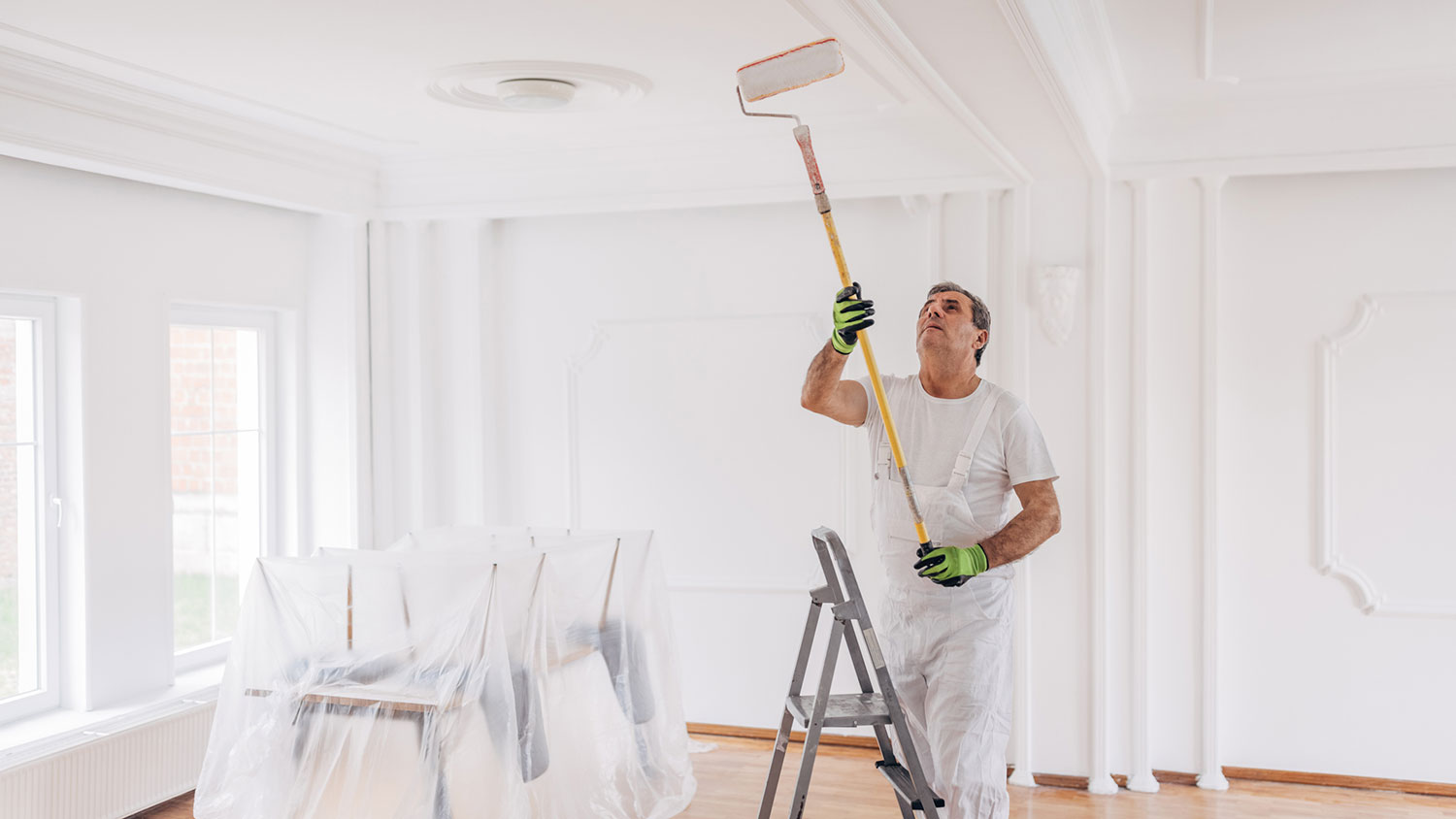 Handyman on a ladder painting living room ceiling