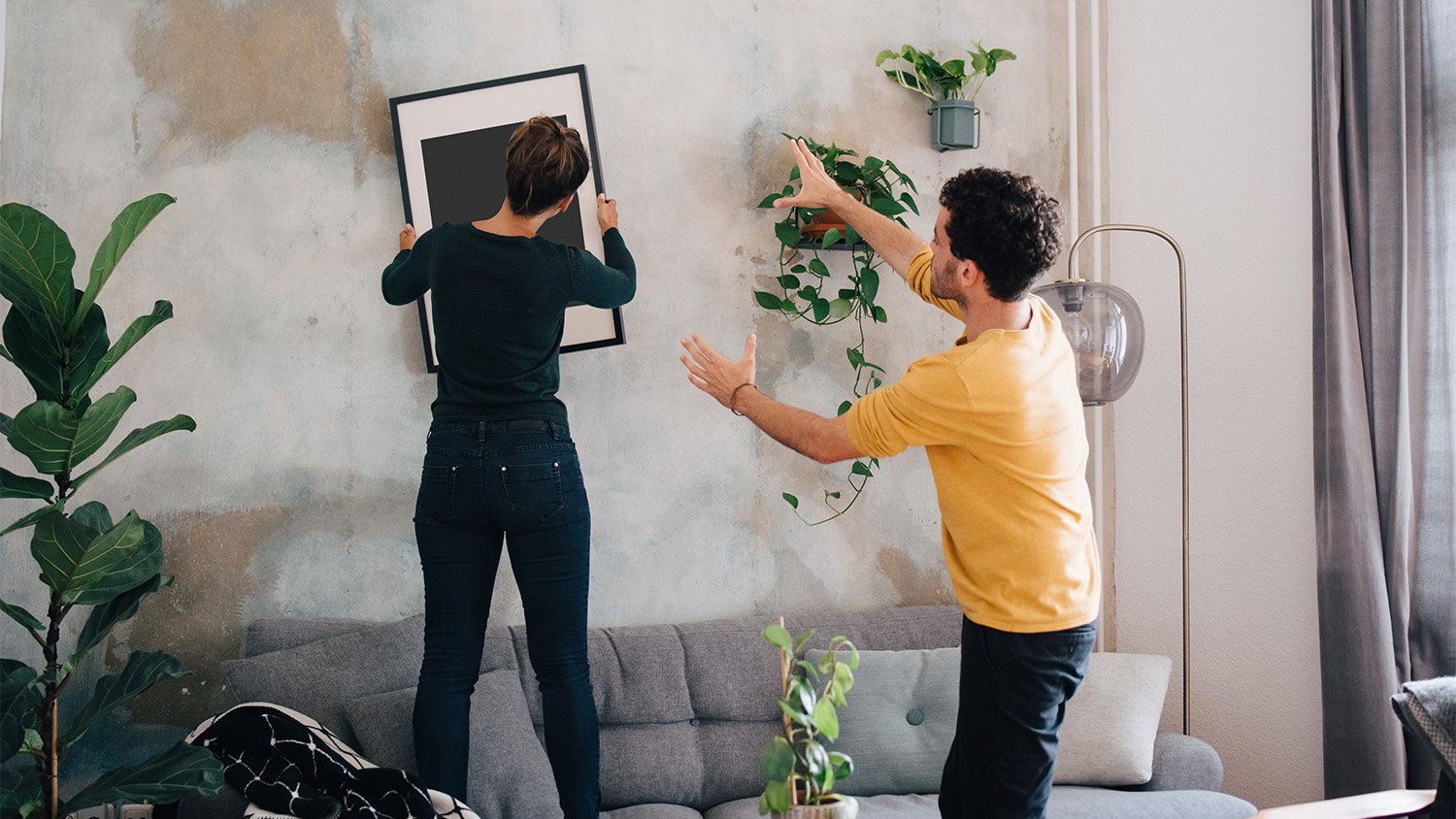 man helping woman straighten painting on the wall of new home