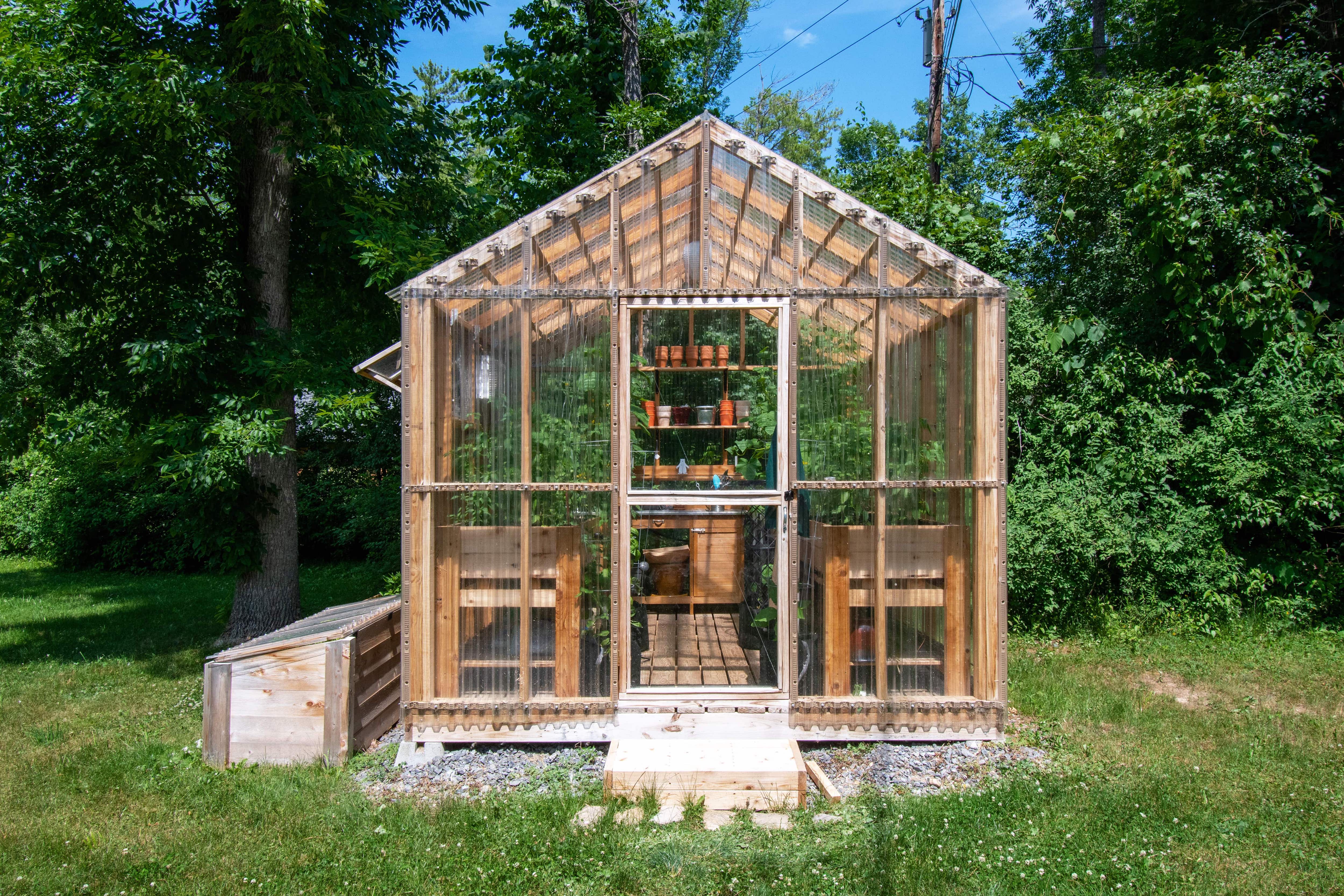 A wooden backyard greenhouse with plastic walls