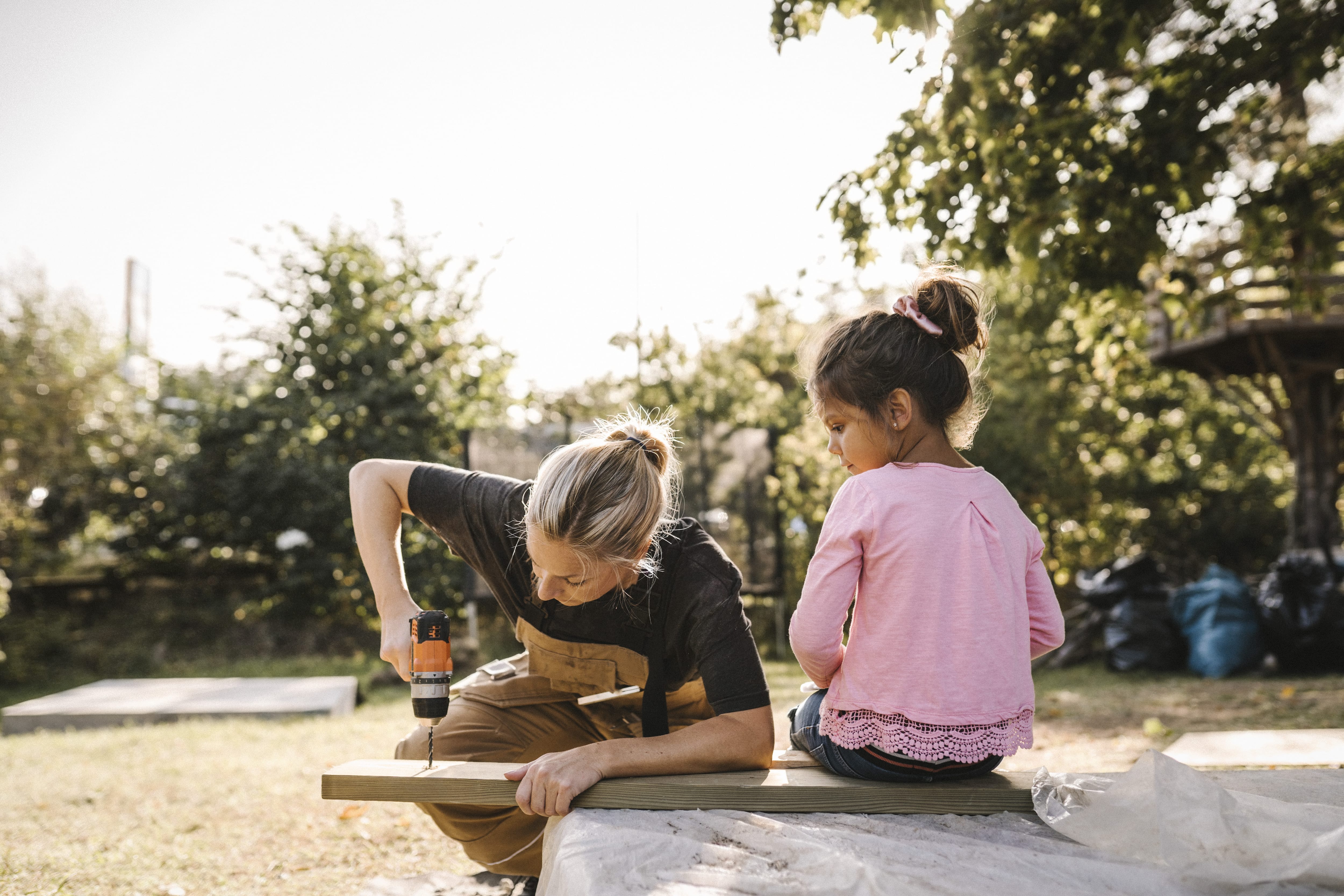 A young girl watching her mom use a drill to build something with wood