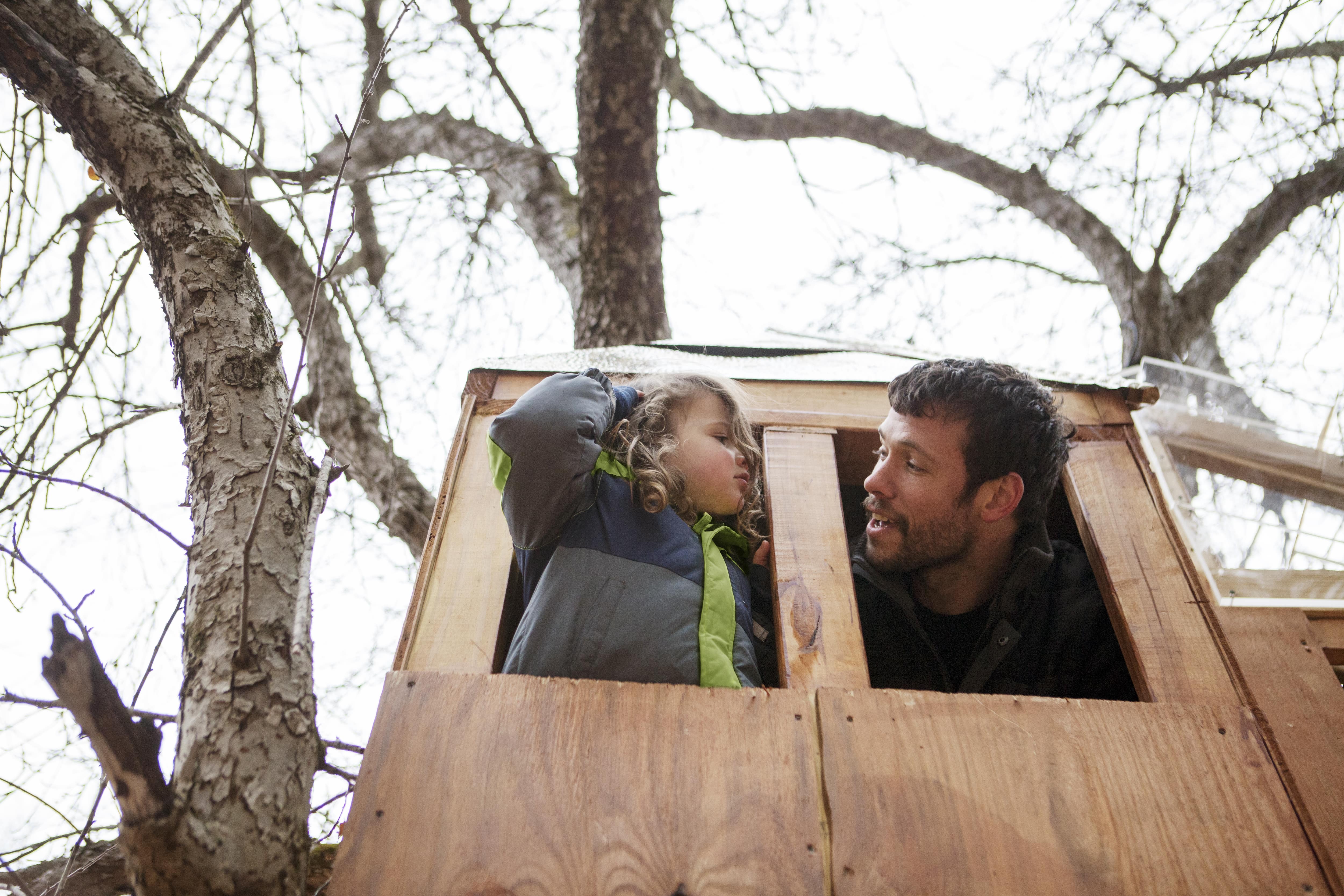 A father and child looking out of a treehouse window 