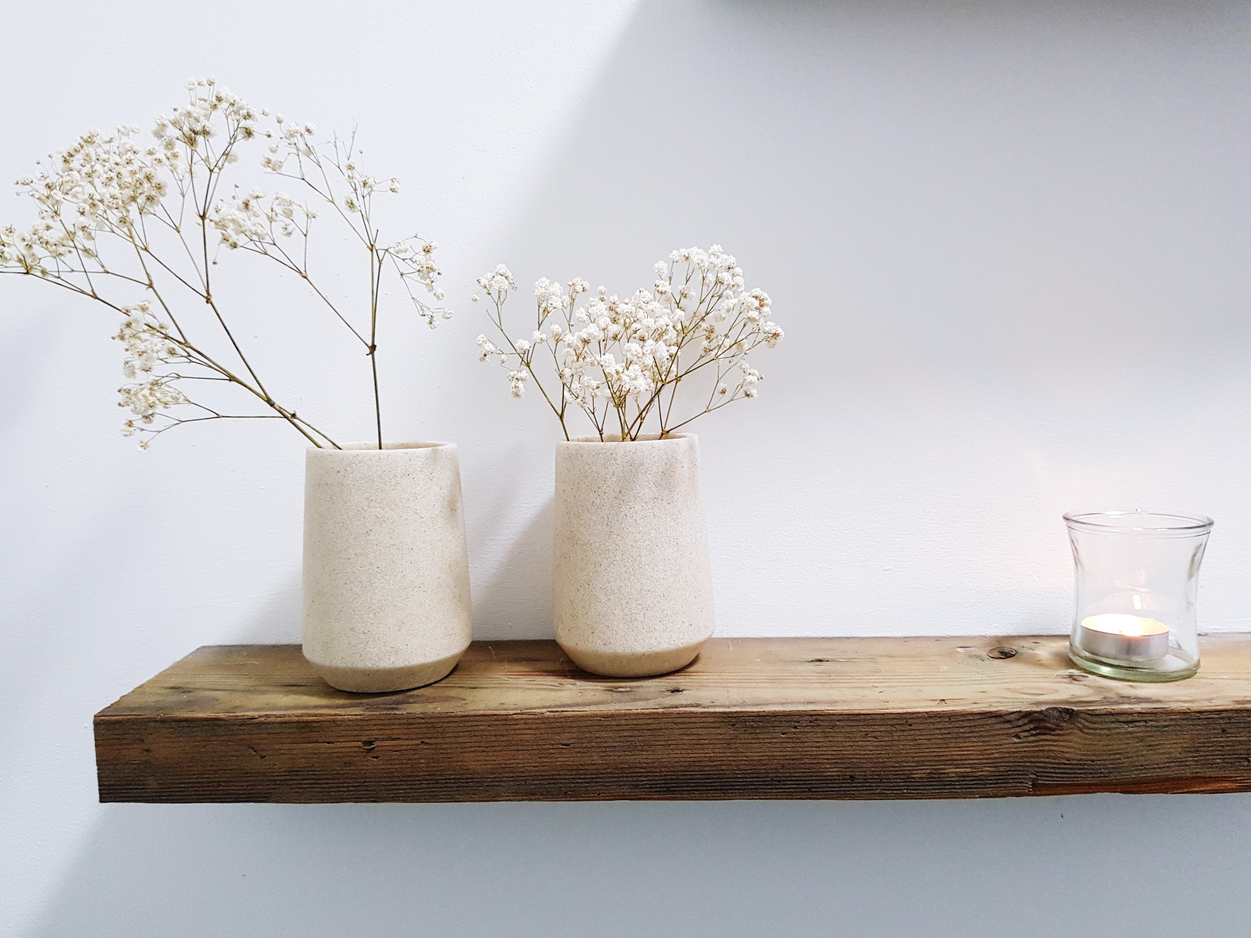 Neutral decor vases with baby’s breath on a wooden floating shelf