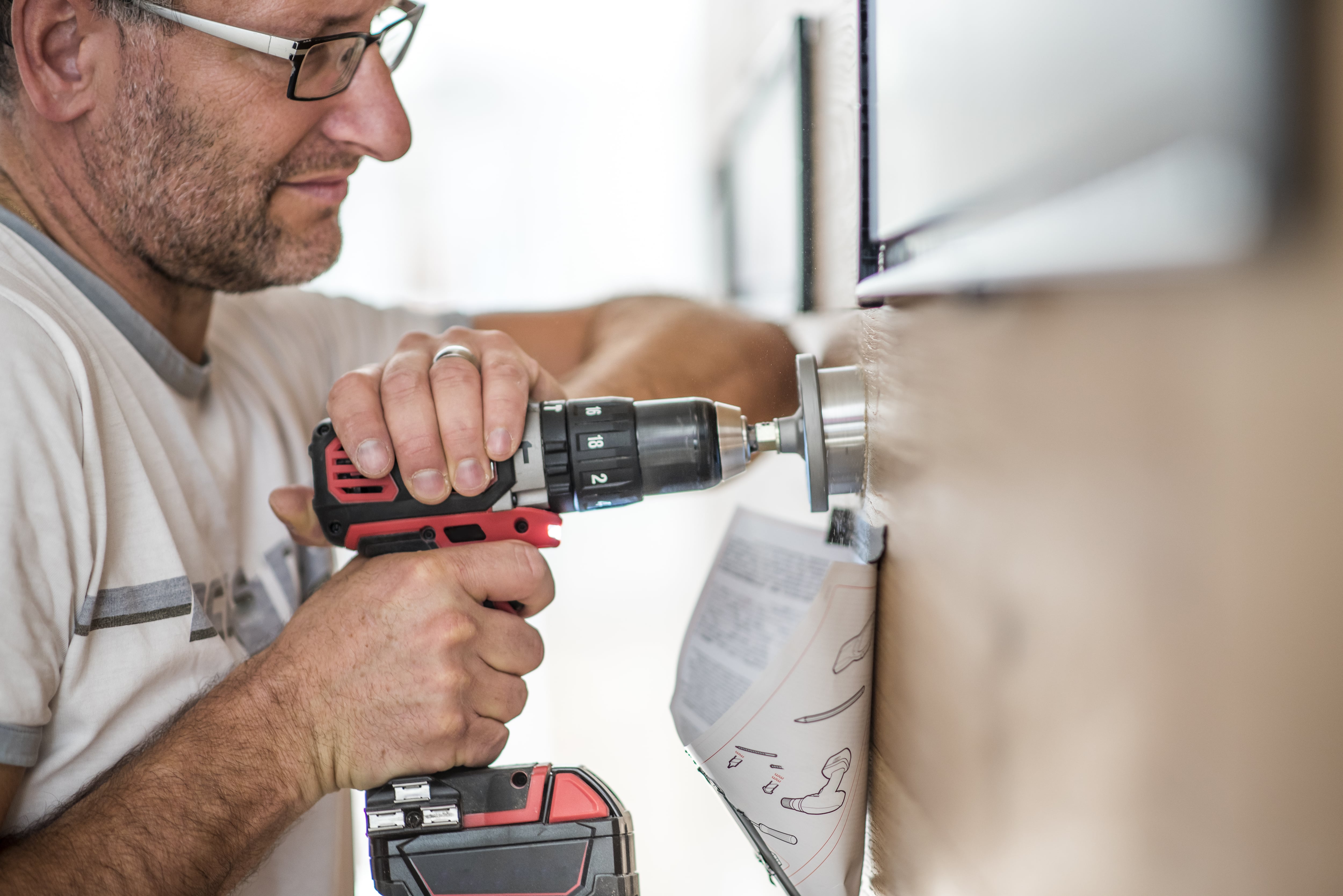 A man using a hold saw drill bit on a wood wall