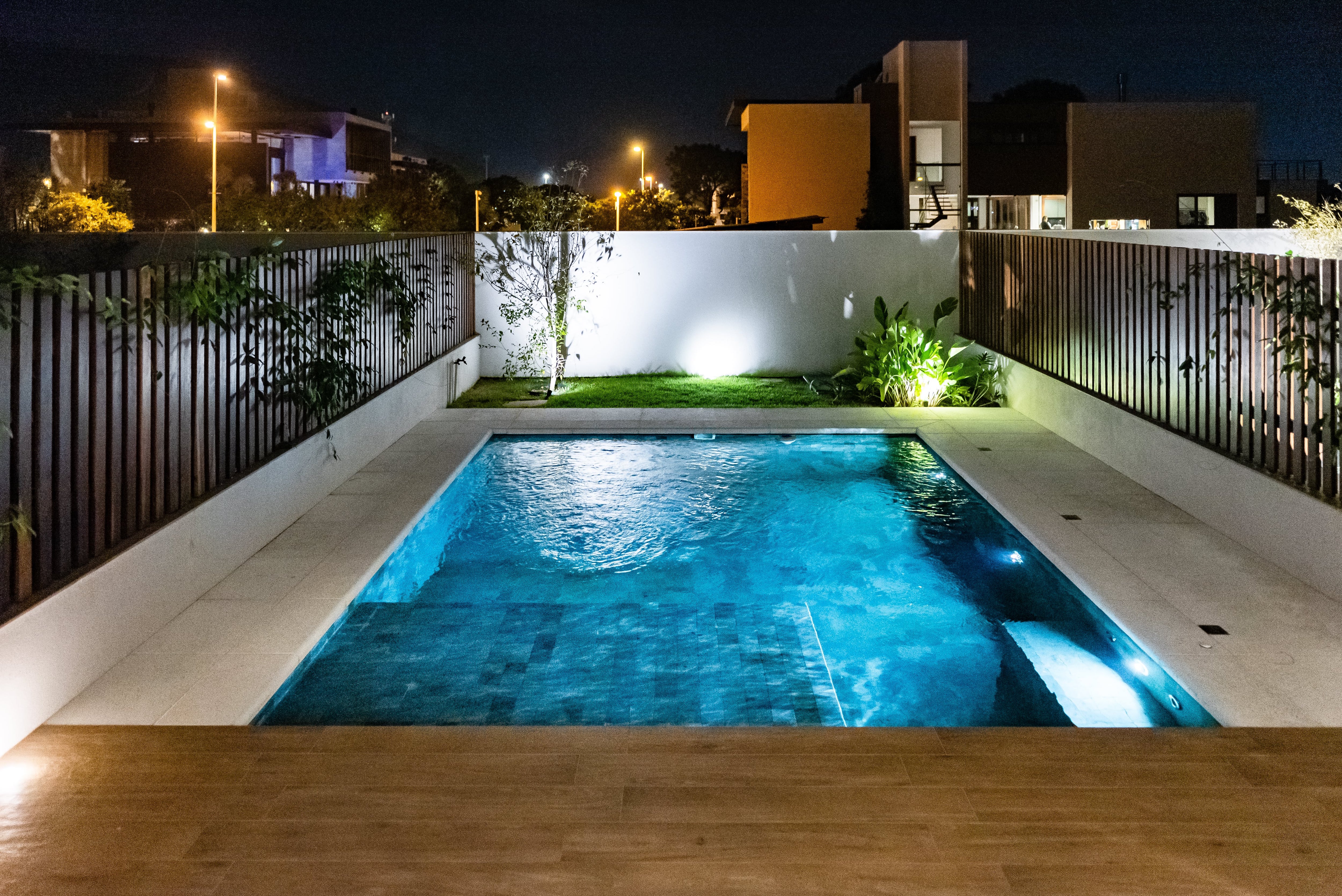 A pool in a small backyard surrounded by concrete and a small patch of grass