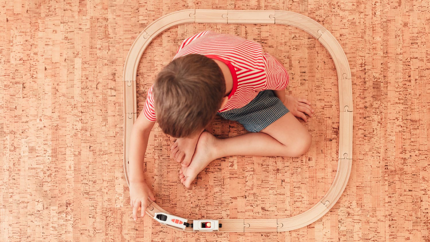 Top view of a kid playing with a toy train while sitting on cork flooring