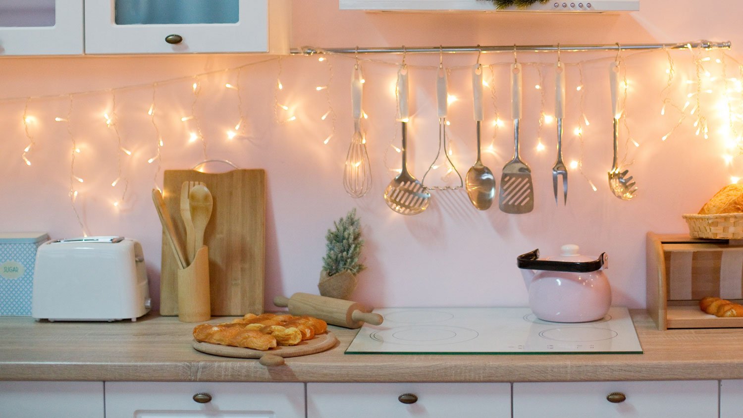 A kitchen with white cabinets, lights and a pink wall