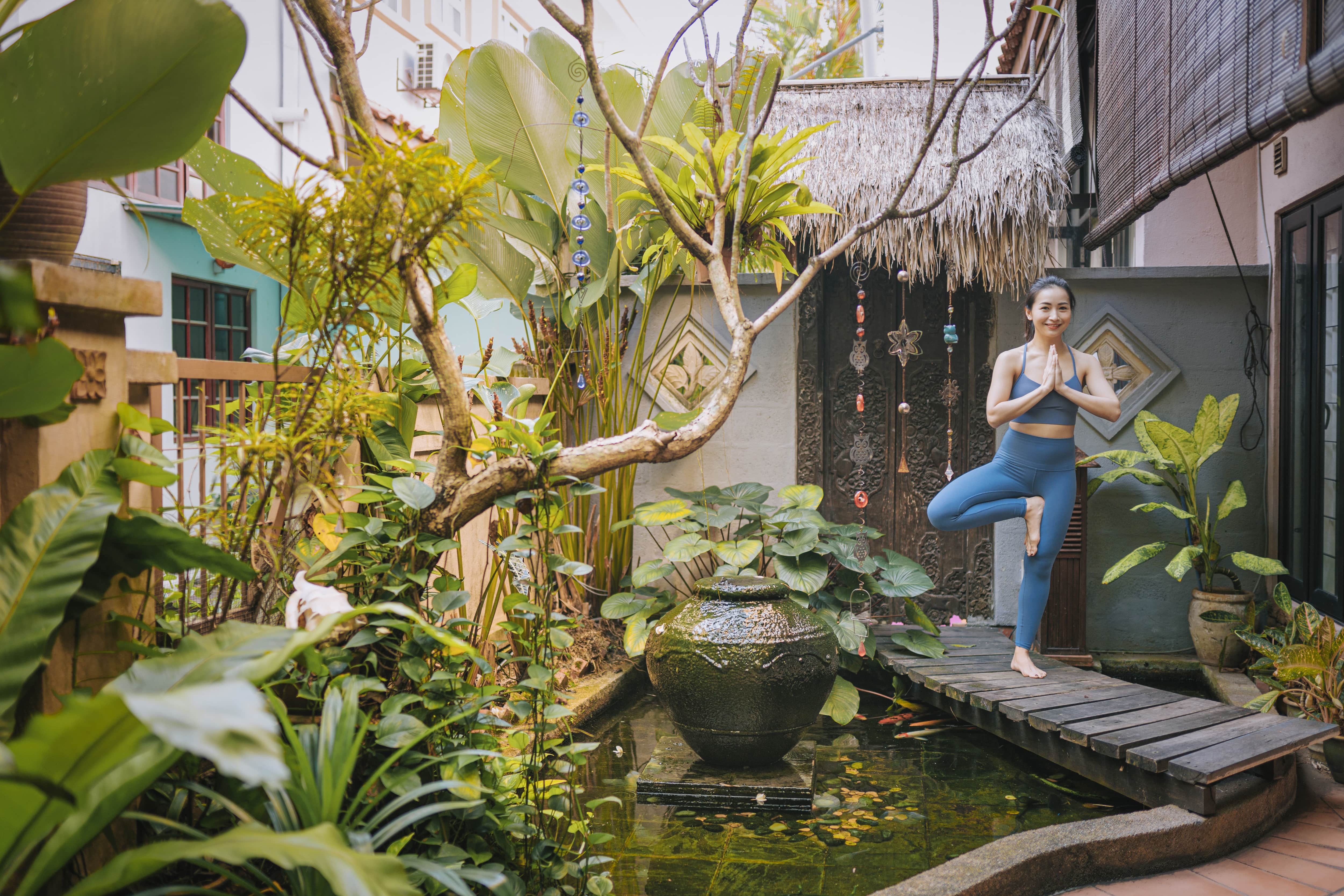 A woman doing yoga on a wood bridge over a koi pond in a small fenced in backyard