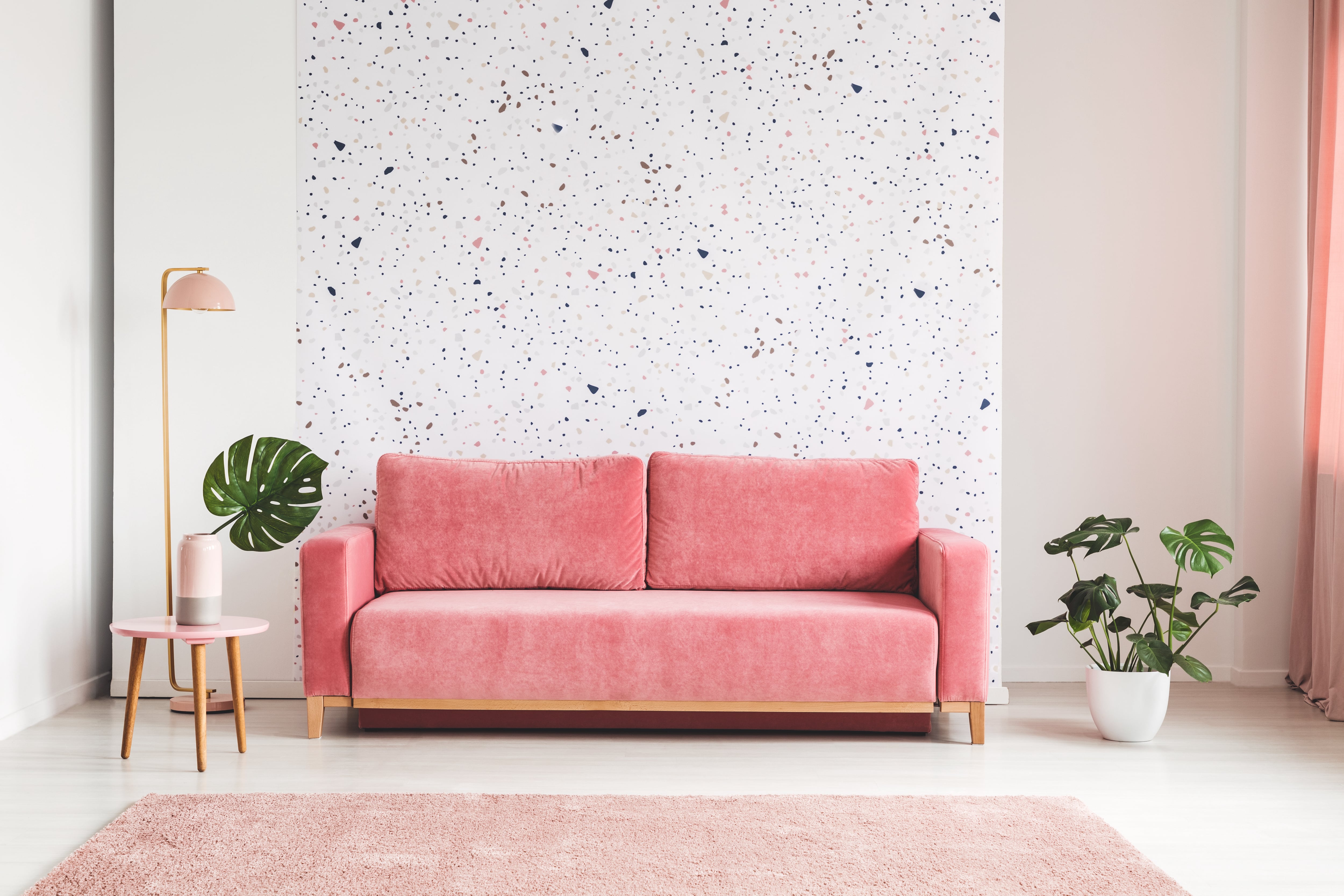 Pink couch with patterned wallpaper behind it 