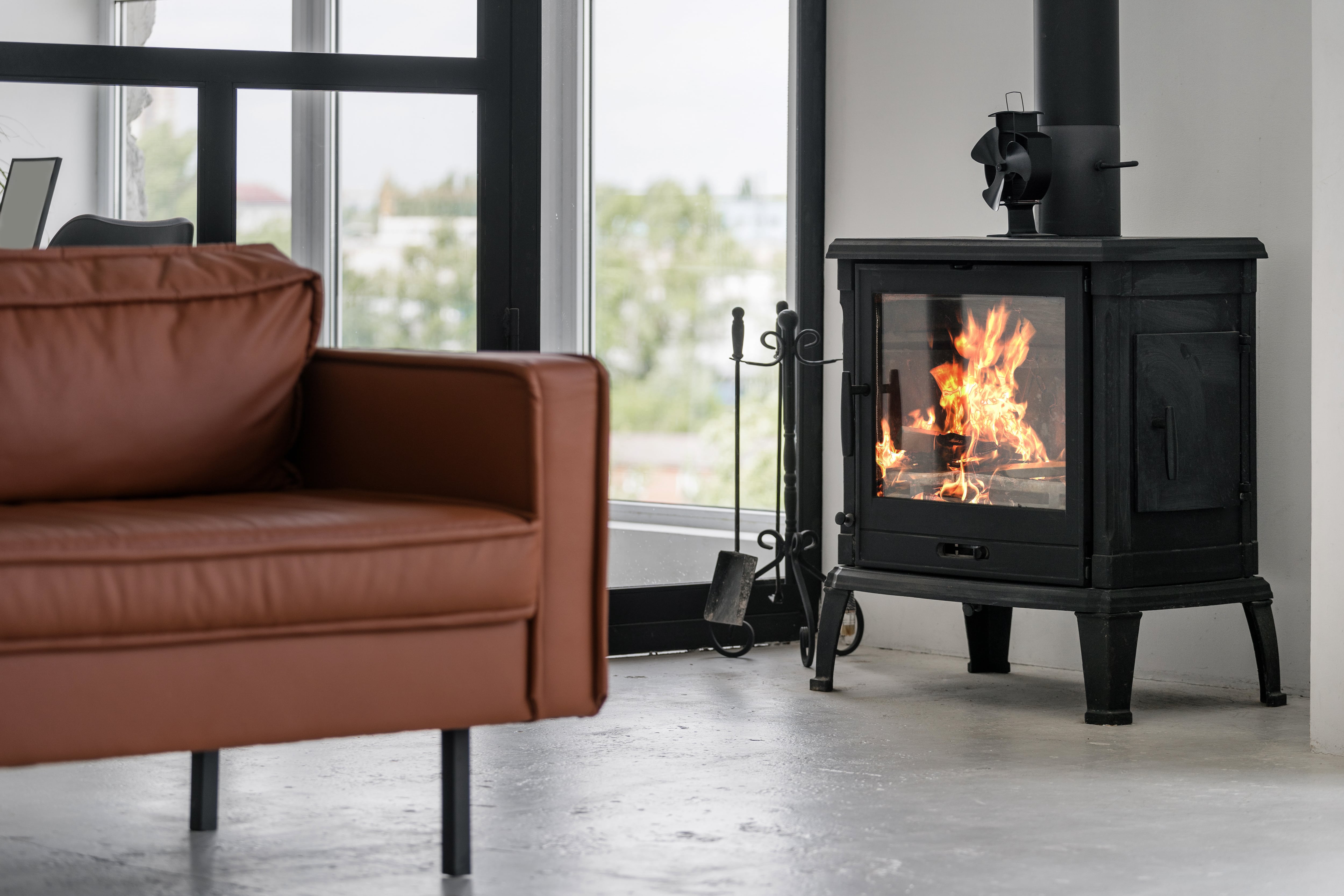 Brown leather couch next to a black wood-burning stove 