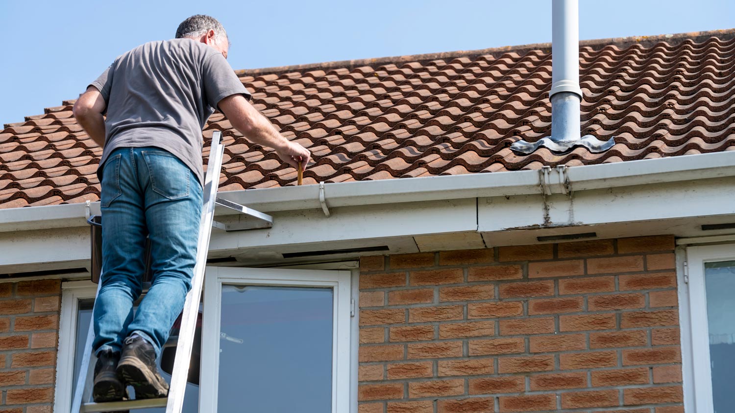 man cleaning leaves from gutter  