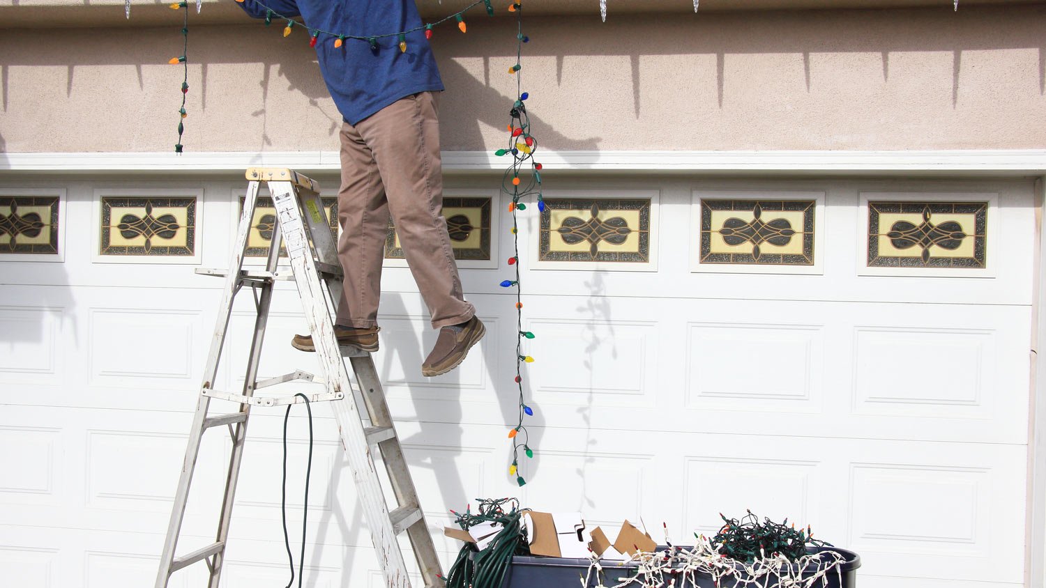 A man on a ladder hanging Christmas lights above the garage door