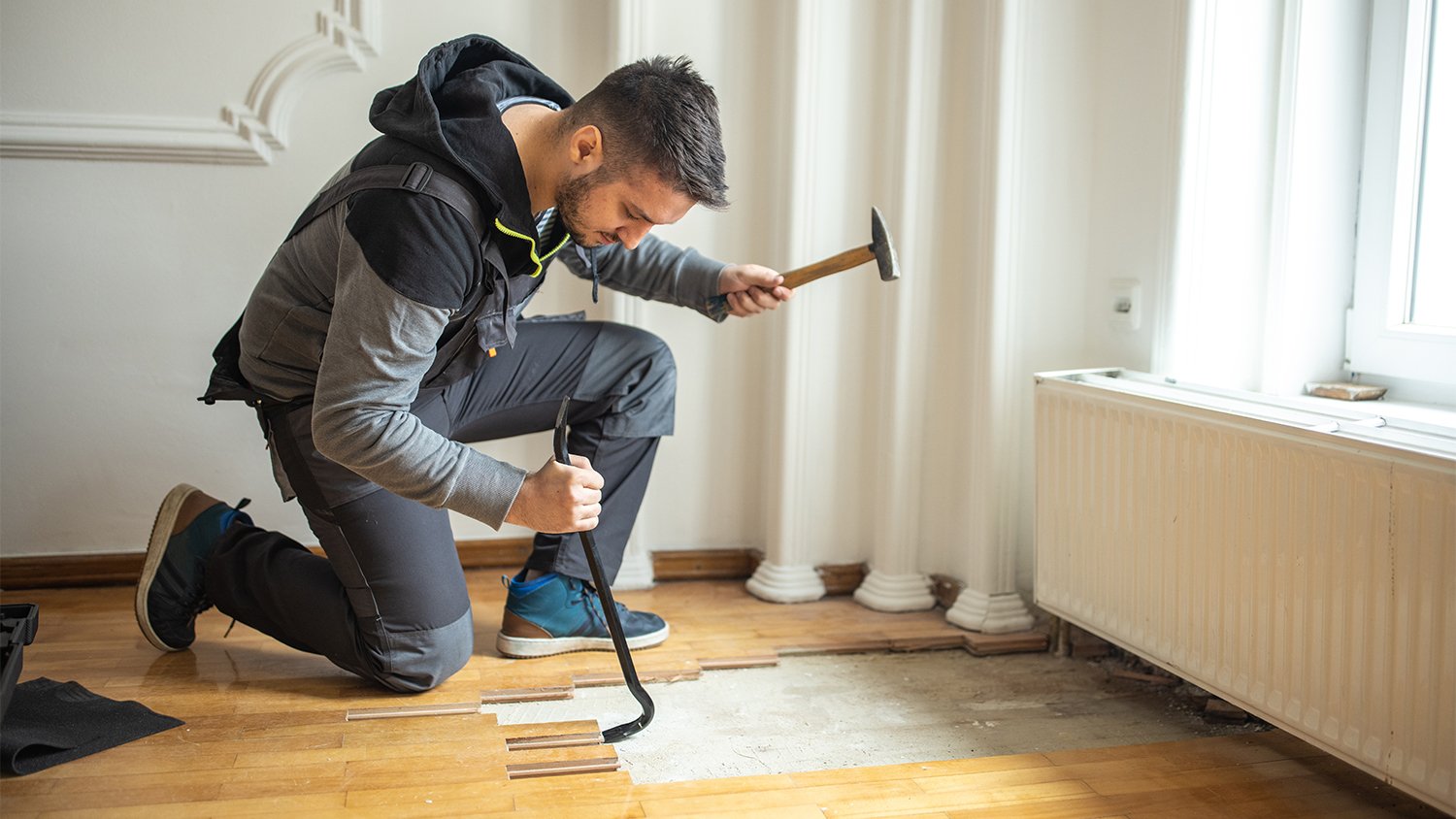 Manual worker removing parquet flooring during home renovation