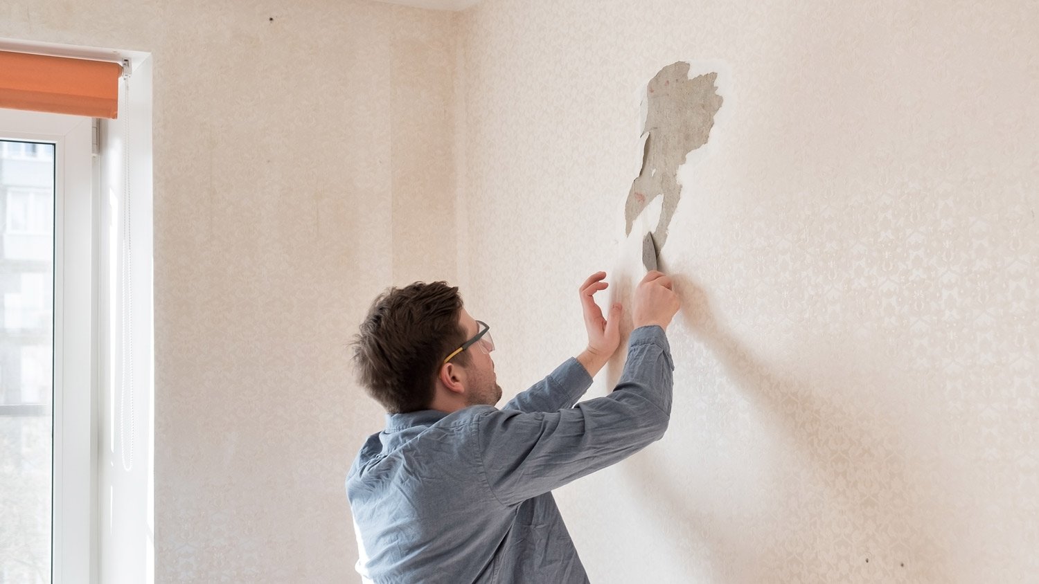 A man removing old wallpaper from a wall