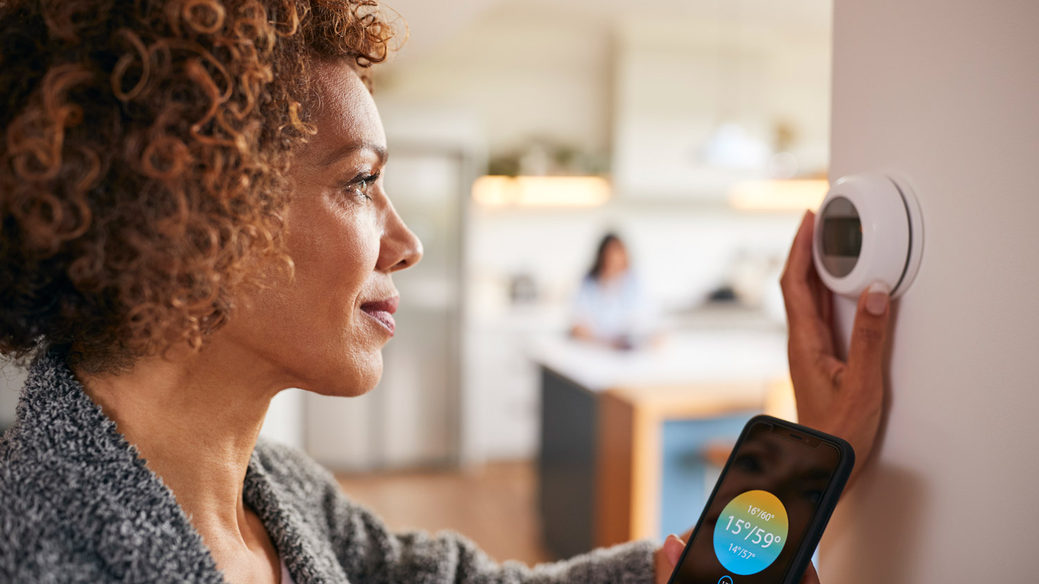 A mature woman adjusting the temperature of the house via a digital thermostat