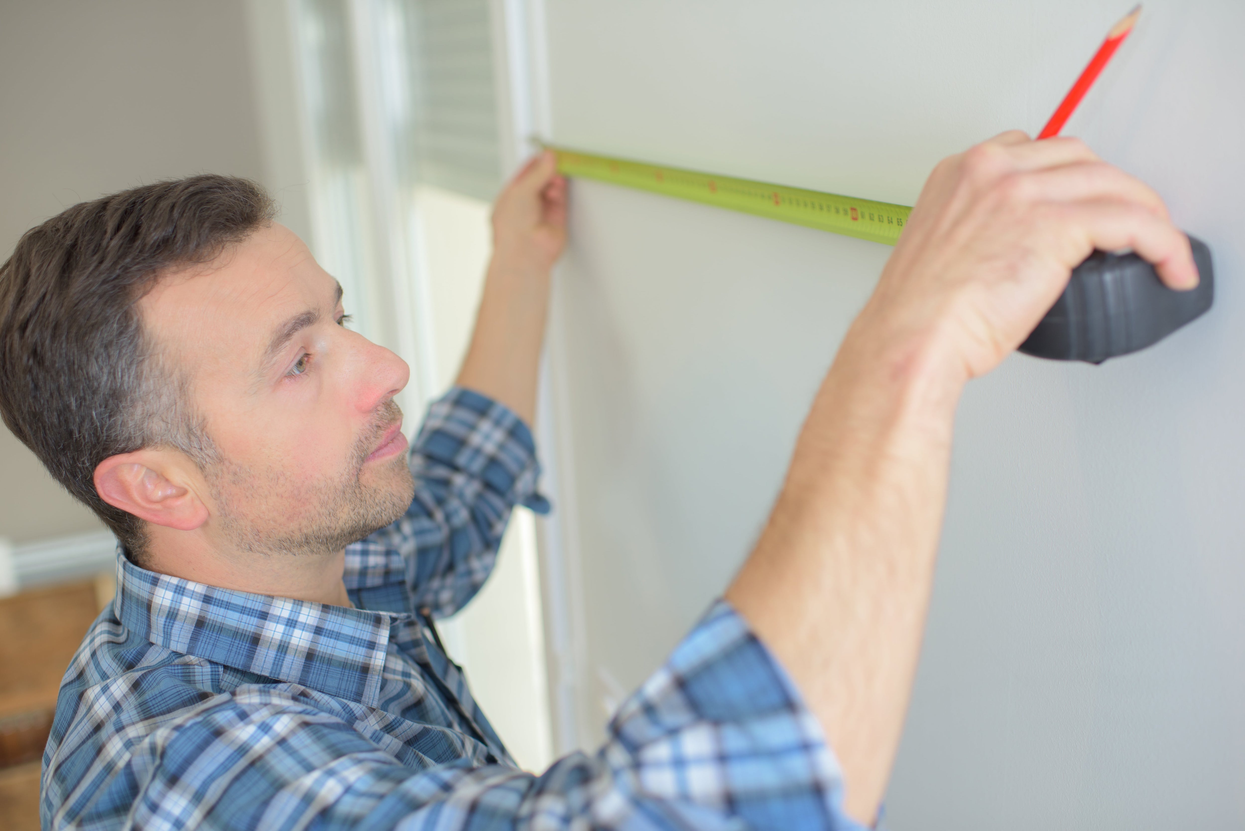 A man measuring a wall with a tape measure and pencil