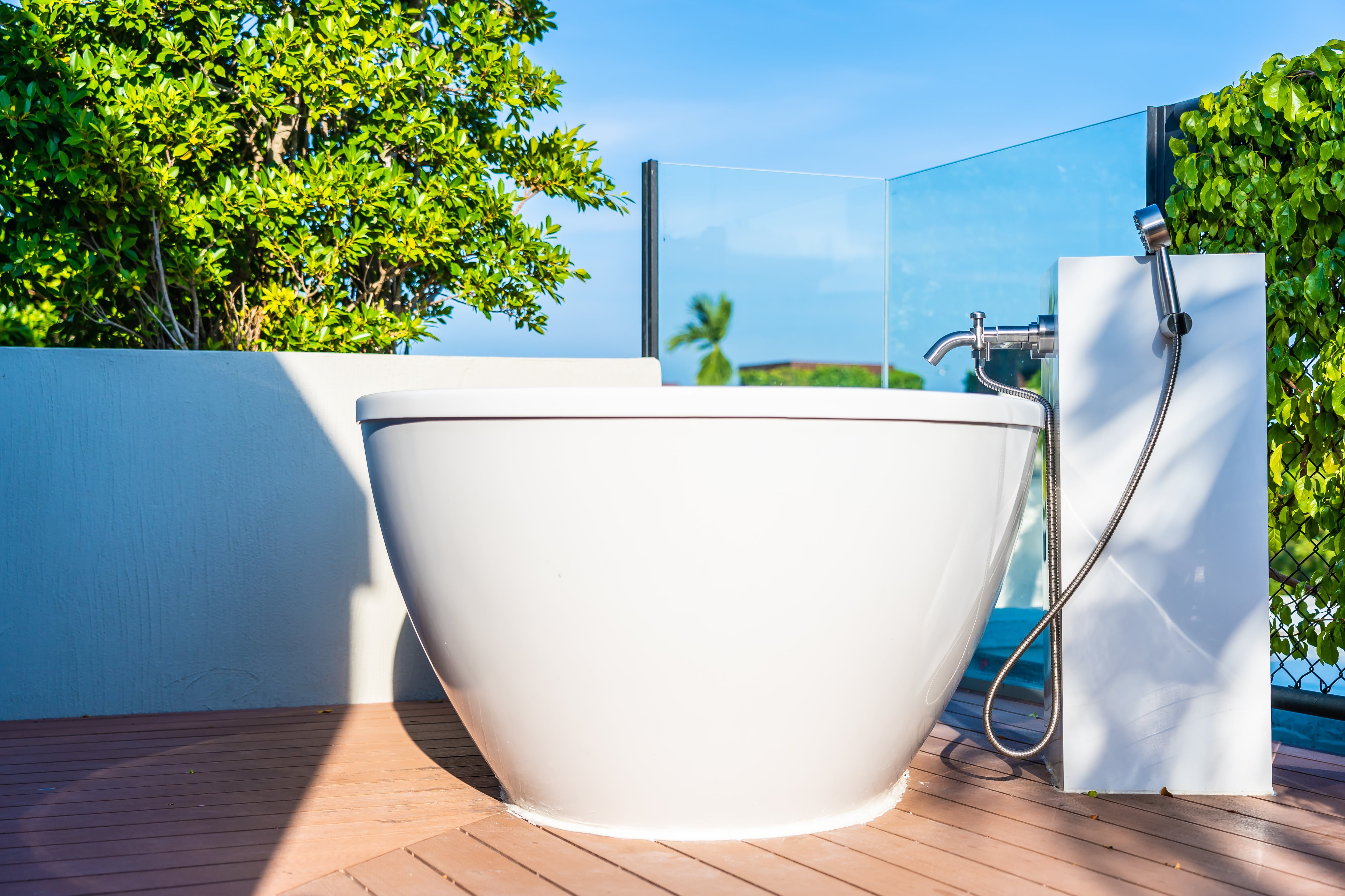 A white soaker tub with a detachable hand-held showerhead on an outdoor deck