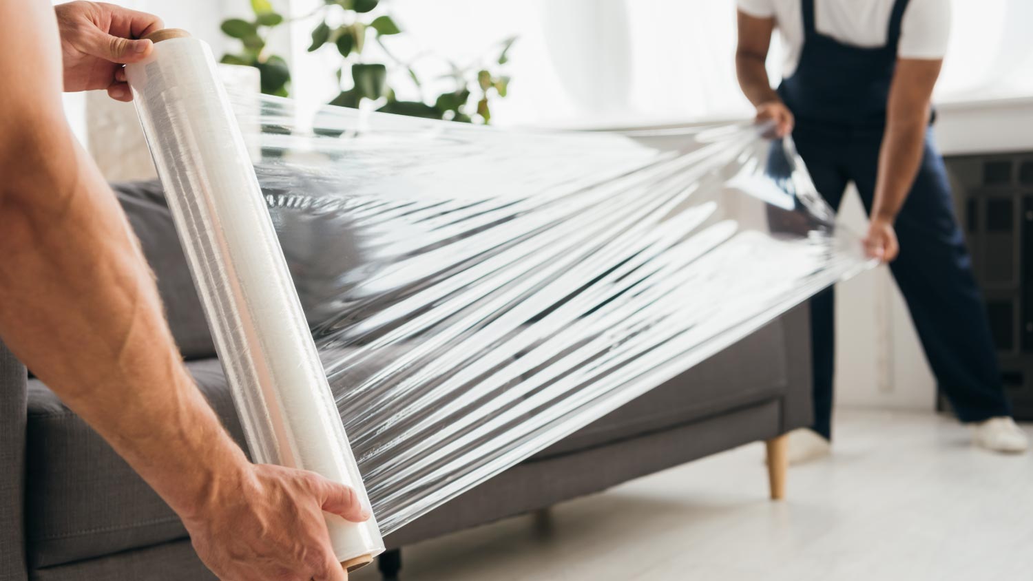 Movers holding stretch film roll near sofa